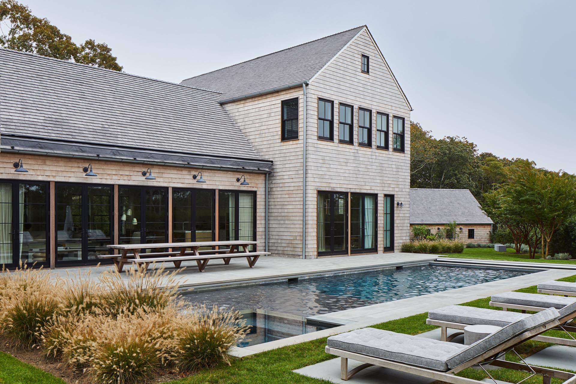 Located in Amagansett, New York, this modern farmhouse inspired home has a wood shingle exterior, as well as a swimming pool and patio.