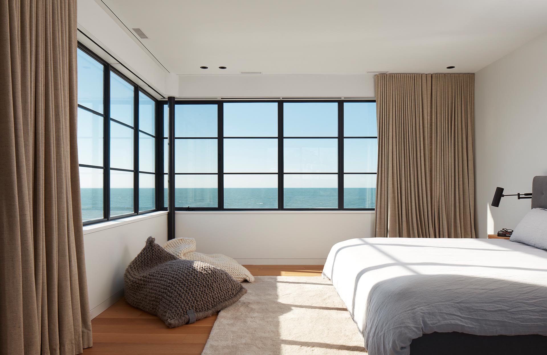 In this modern bedroom, the black-framed windows wrap around the corner of the bedroom, flooding the room with natural light during the day.