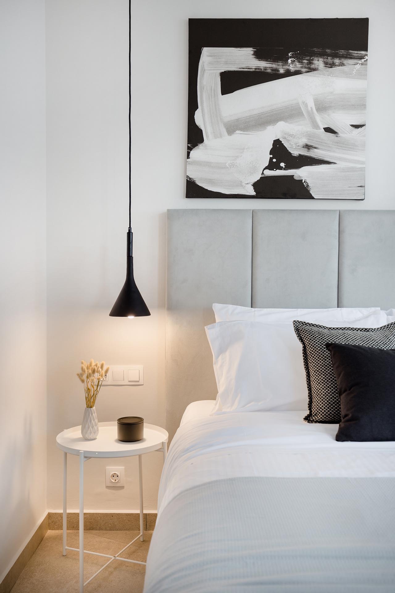 A modern bedroom where the color palette is filled with grays, black and white. At night, the pendant lights beside the bed add a warm glow.