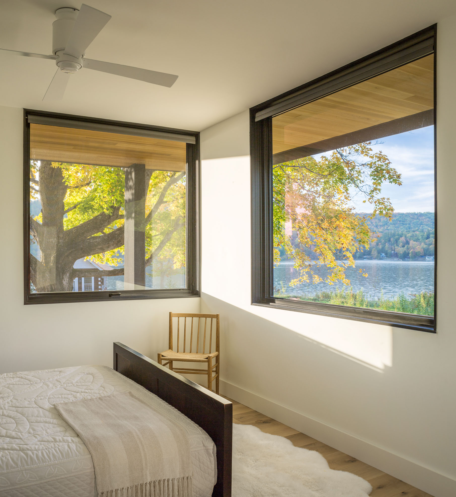 In this modern bedroom, black framed windows on two walls look out to the lake and trees.