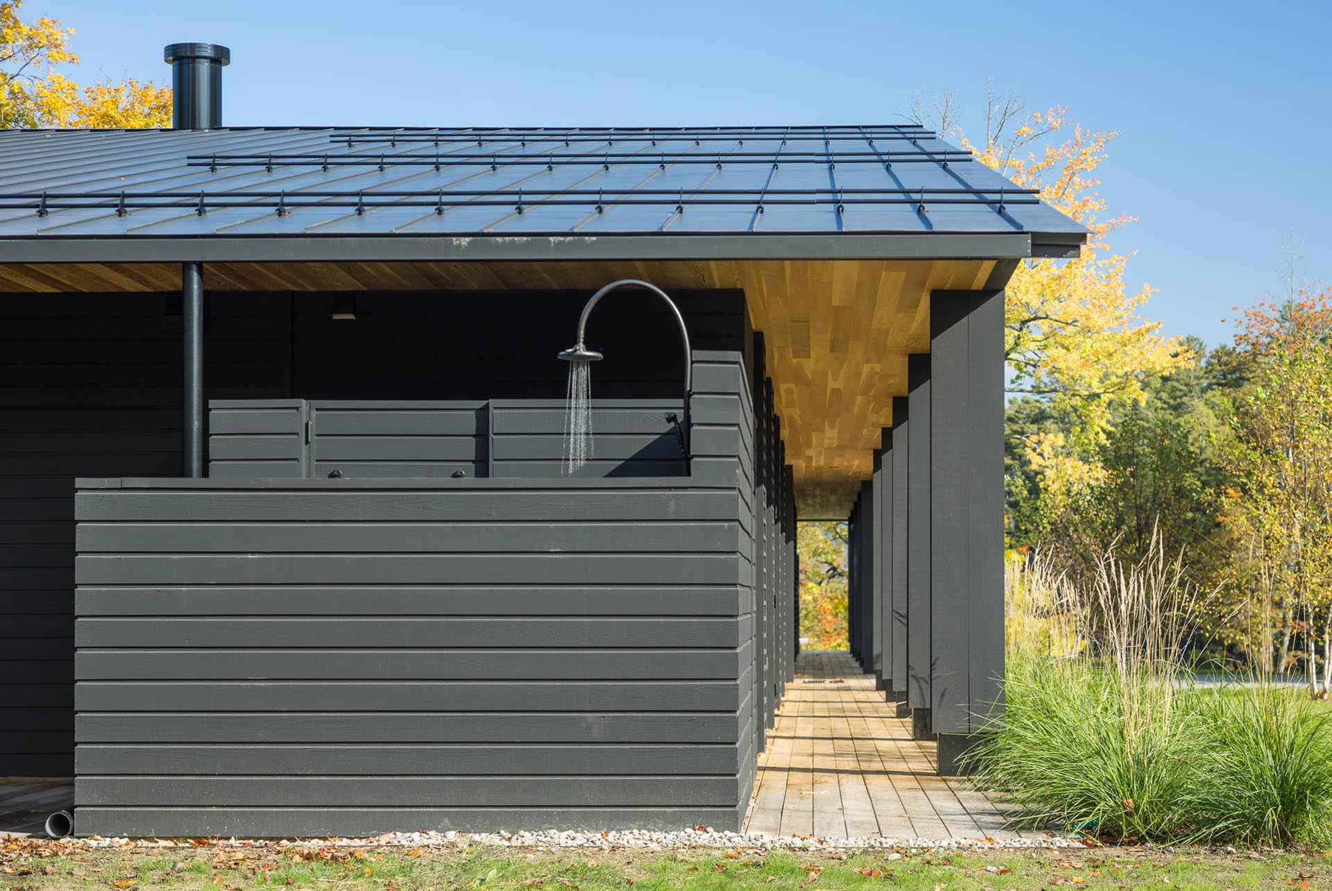 A modern house with black exterior siding, a black metal roof, and an outdoor shower.