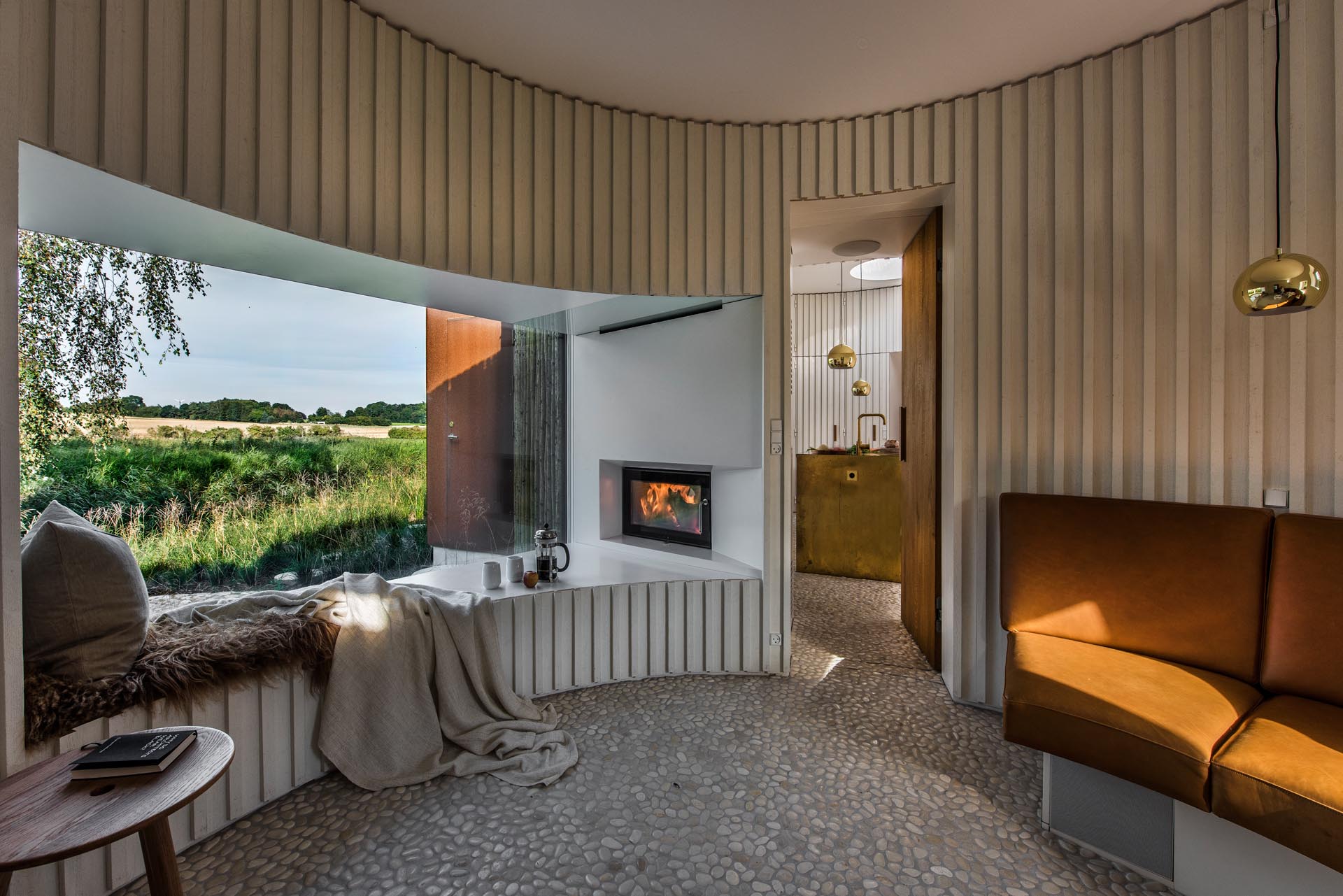 A curved modern living room with a large window seat that also has a fireplace at one end.