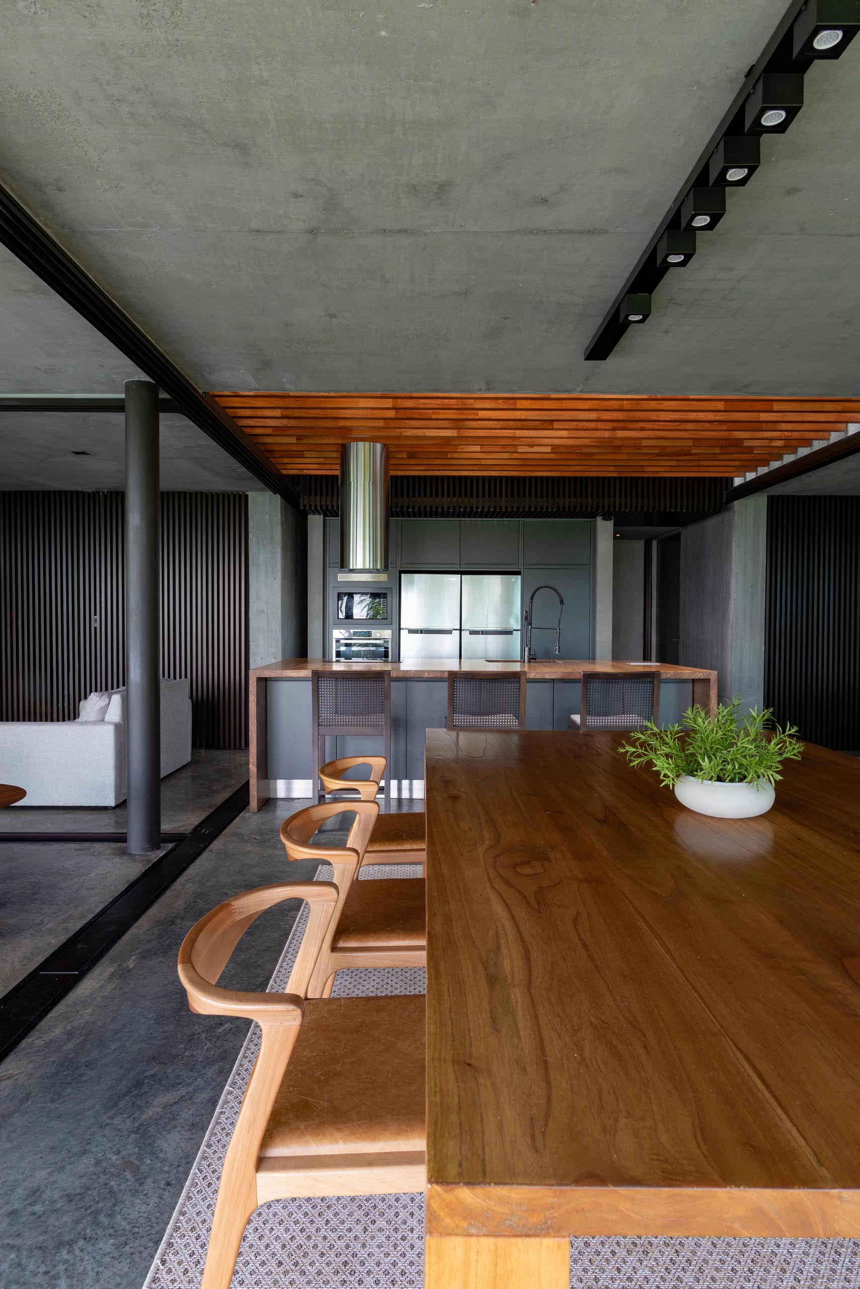 A modern open plan interior that includes a dining room with large wood table, and a kitchen with matte black cabinets.