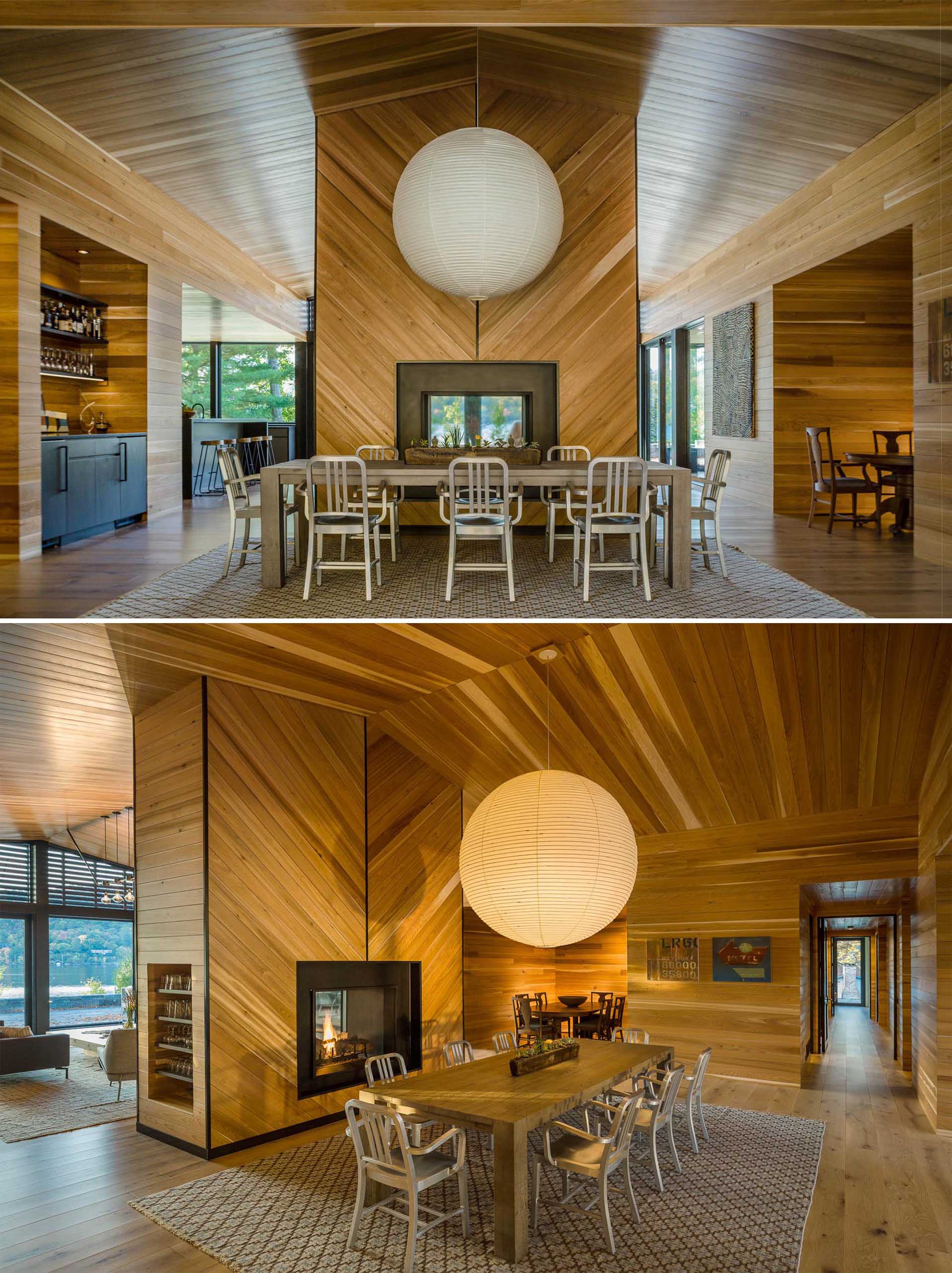 This dining room has a wood table that sits below an extremely large pendant light with a white shade. The dining room also enjoys a nearby recessed bar area as well as a double sided fireplace.