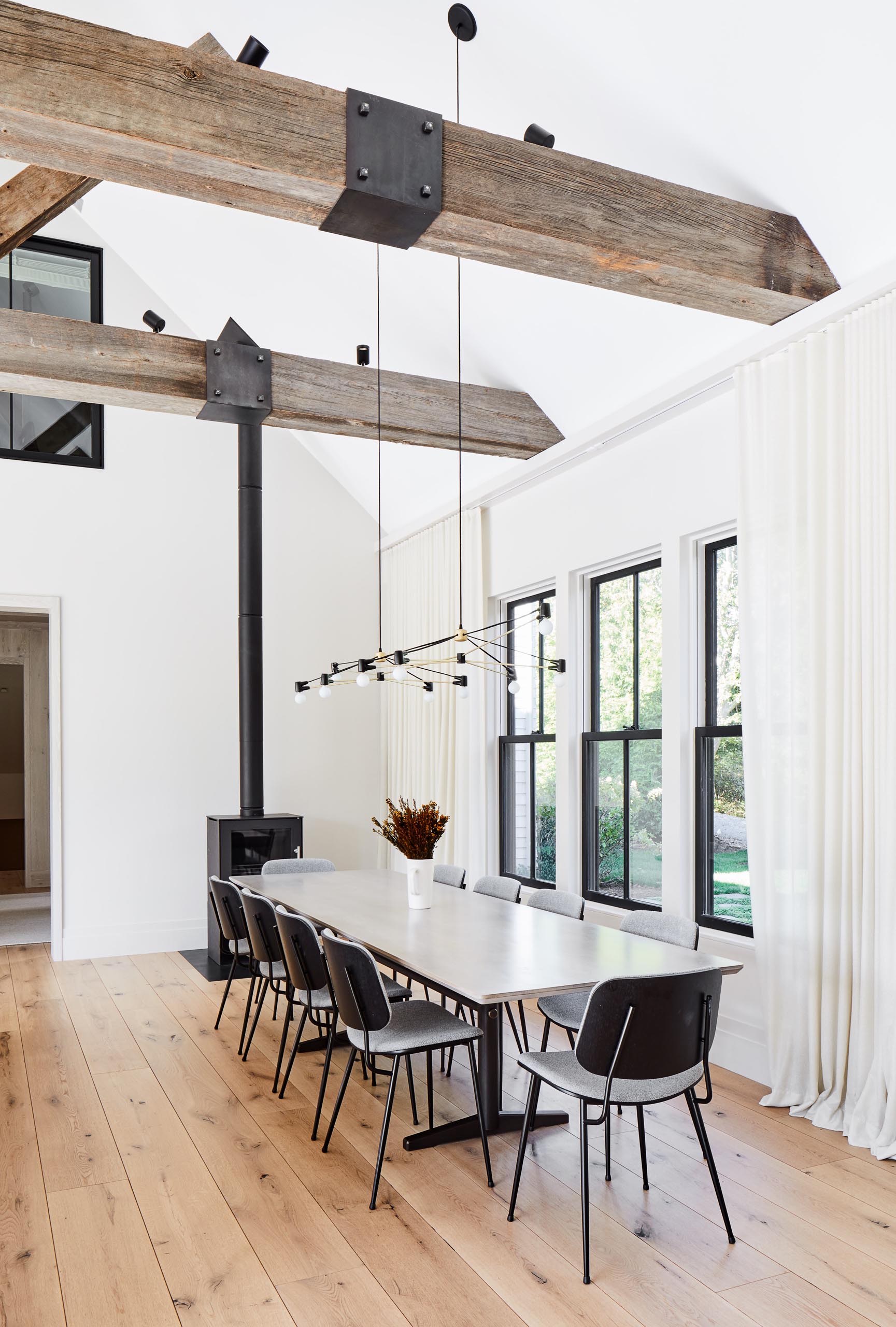 This modern farmhouse dining room features the Double Cord Chandelier from Brendan Ravenhill Studio, which extends over the large dining table. Throughout the home there's solid wide plank white oak from The Hudson Company with a clear Bona Traffic finish.