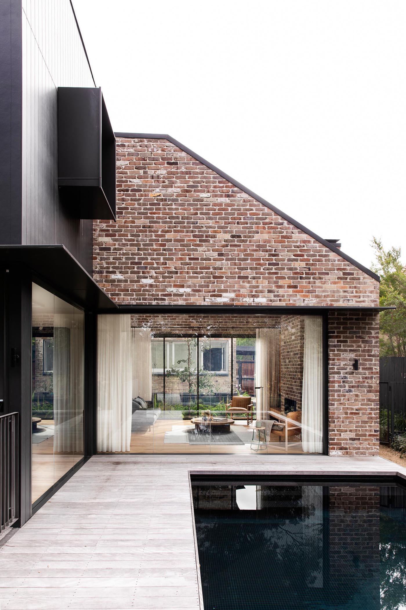 An additional glass wall in living room of a new home new addition provides views of the pool, while the opposite wall opens to a small courtyard with water-wise Australian native plants.