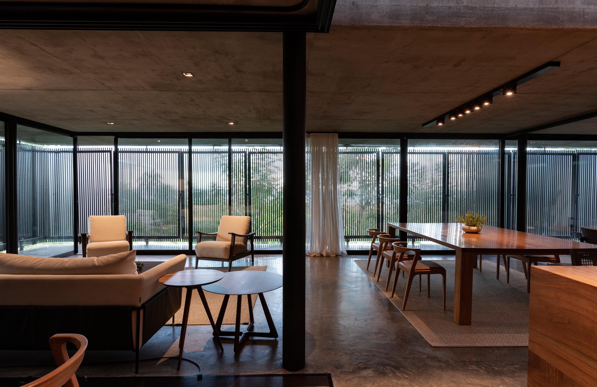 A modern house with an open floor plan, black wood slat screens, glass walls, and concrete floors.