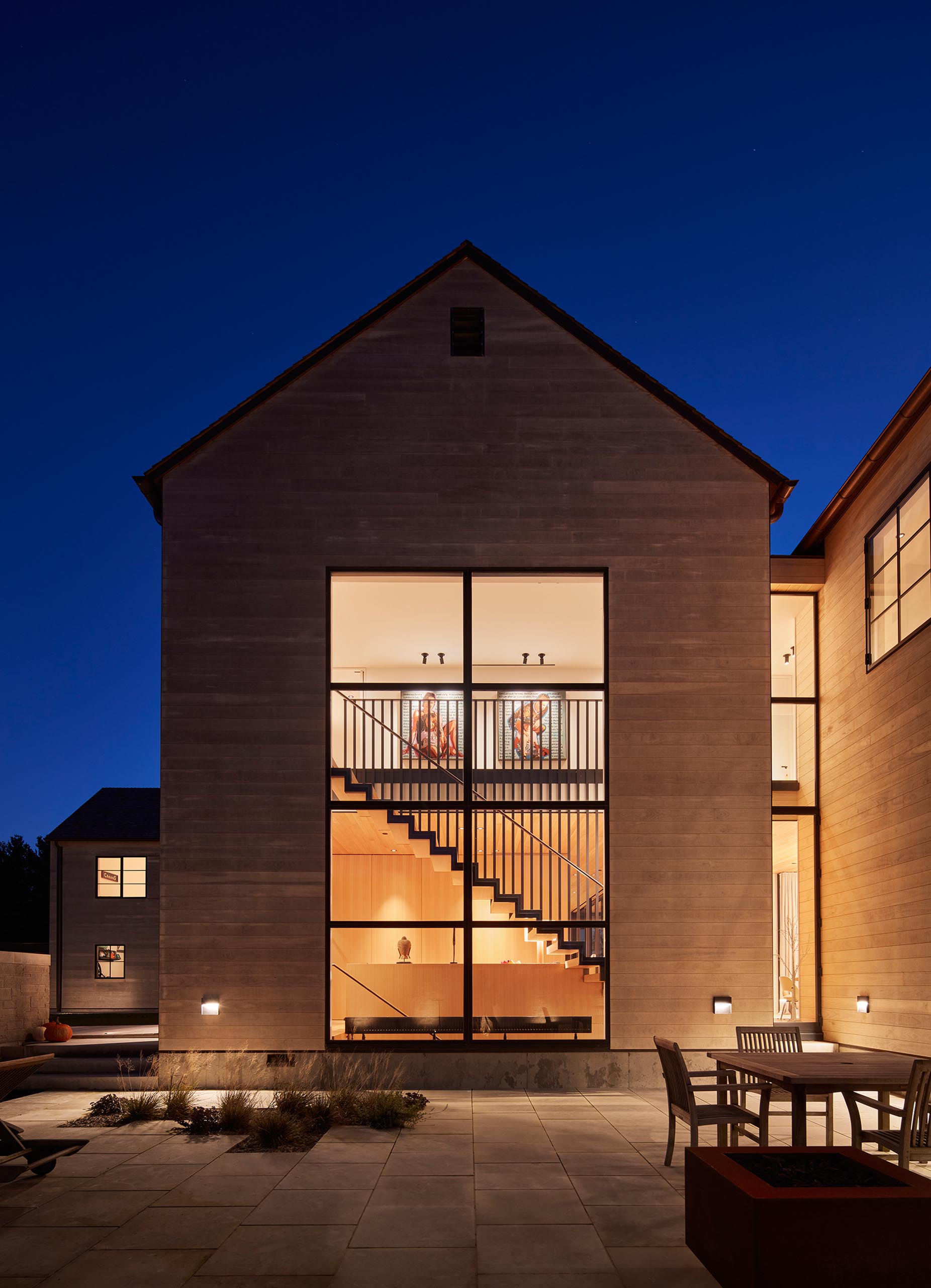 Large windows showcase a steel and wood staircase inside the home.