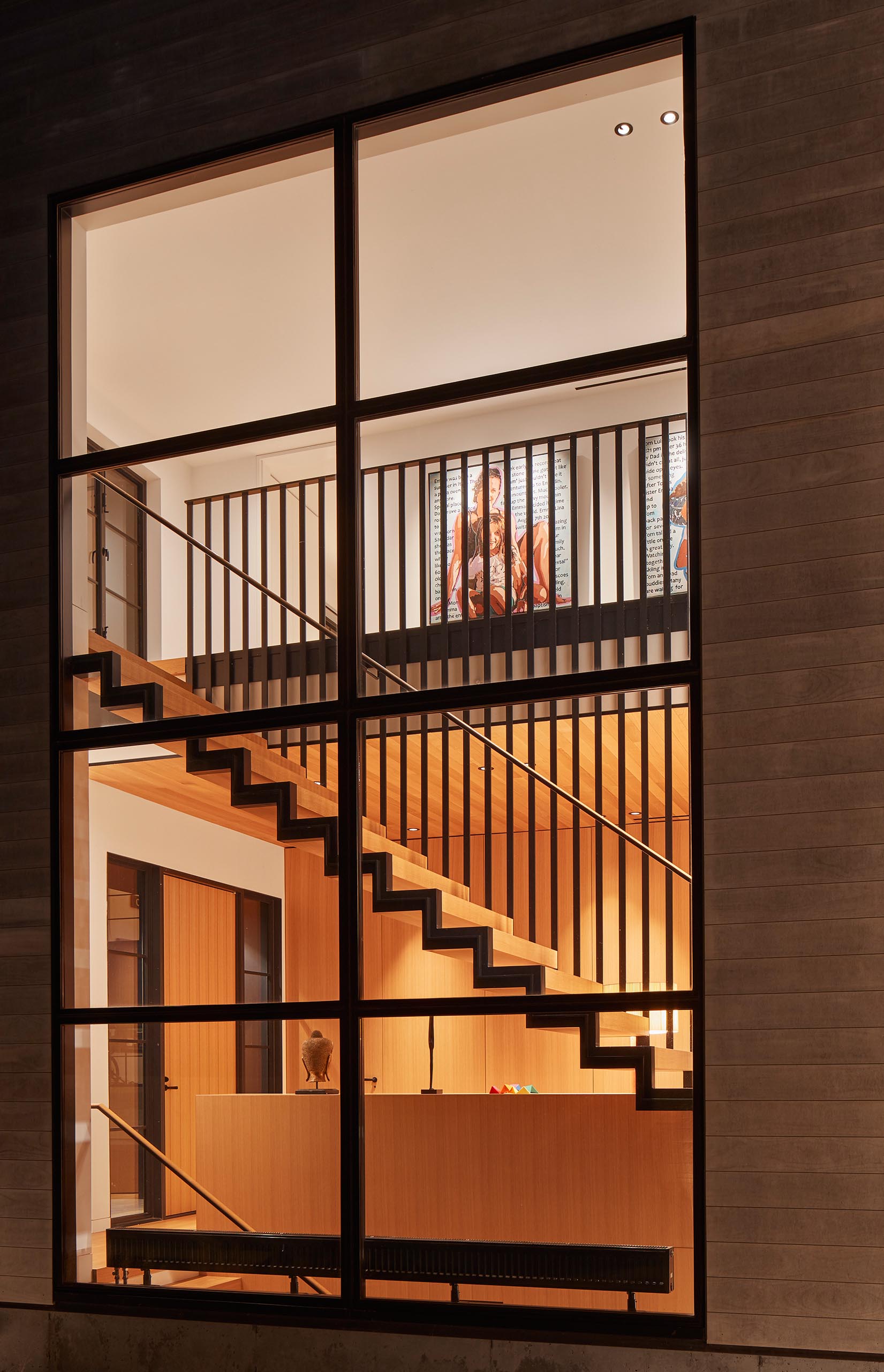 Large windows showcase a steel and wood staircase inside the home.