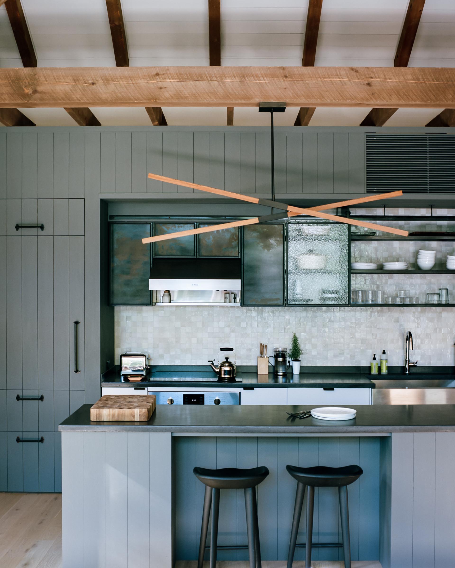 A modern gray kitchen with integrated fridge, dark countertops, black hardware, and an island.