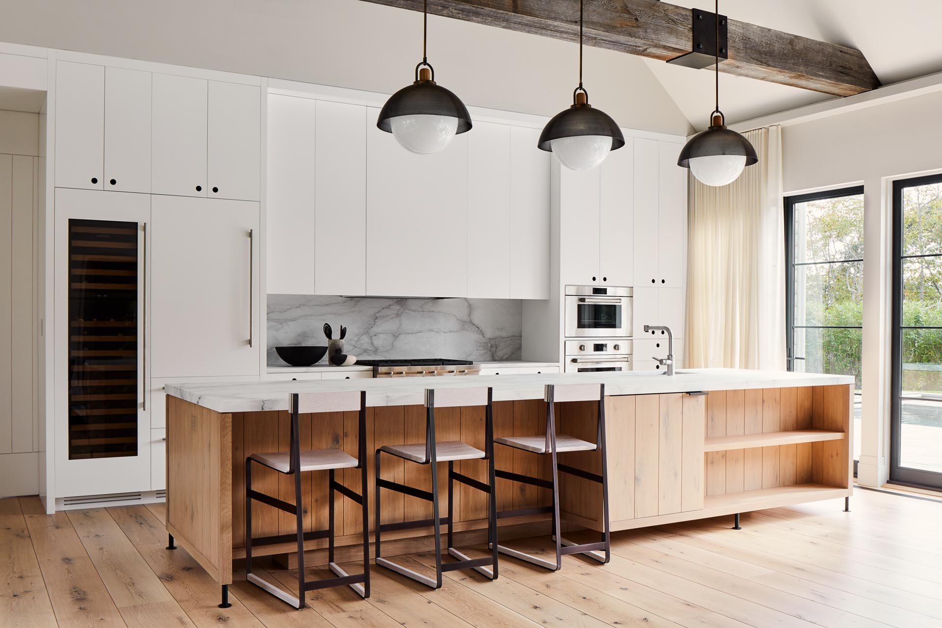 In this modern farmhouse kitchen kitchen, the exhaust fan is concealed within a fixed panel which is flanked by white cabinets. For the cabinets left and right of the stove, the doors hang down below the cabinets so they can be opened by pulling the bottoms of the cabinet doors.