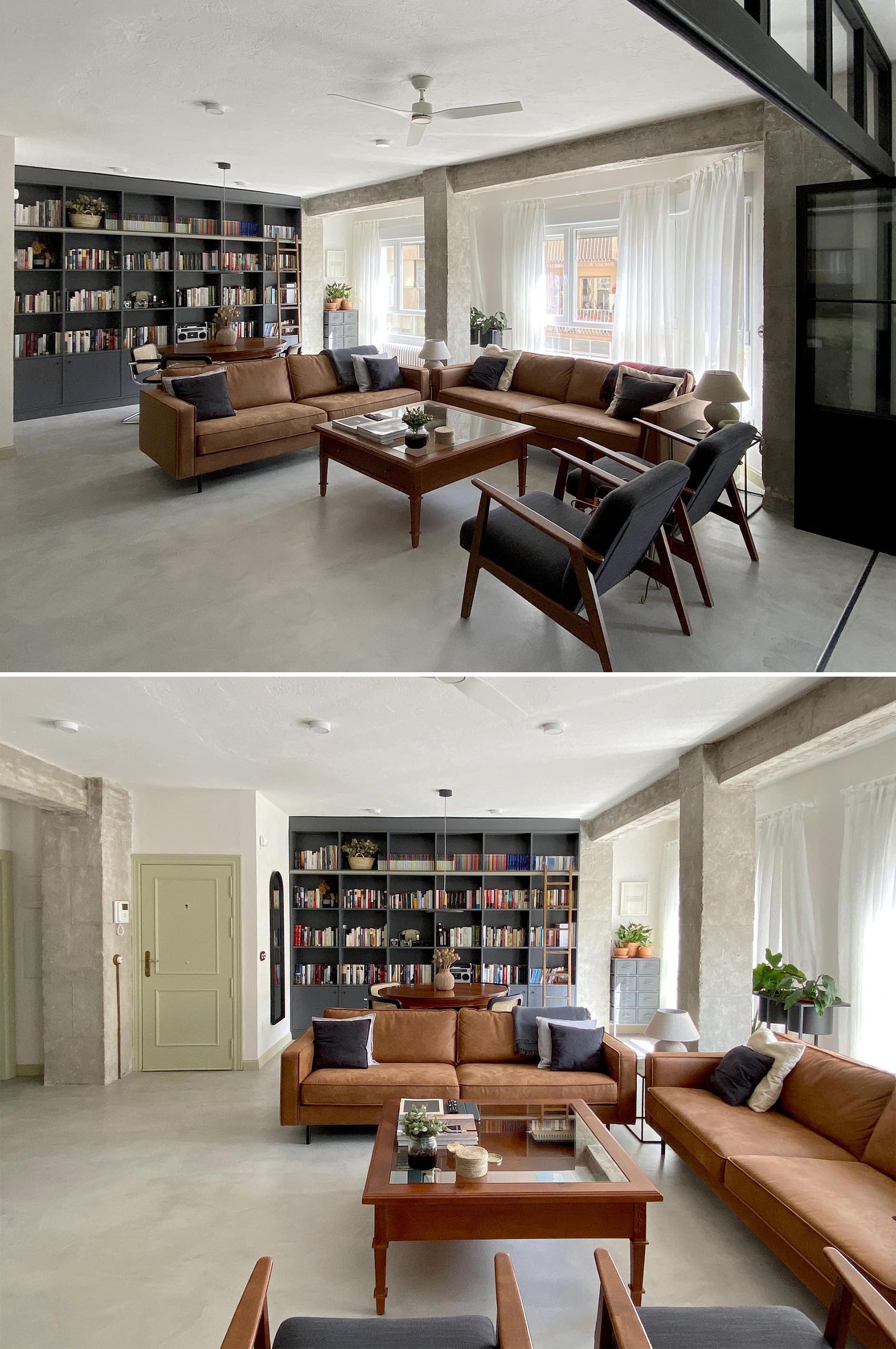 This modern living room showcases the concrete flooring, and is furnished with leather couches, a pair of armchairs, and a wood coffee table. On the living room wall, there's a low console and glass front cabinet that complements the black framed doors.