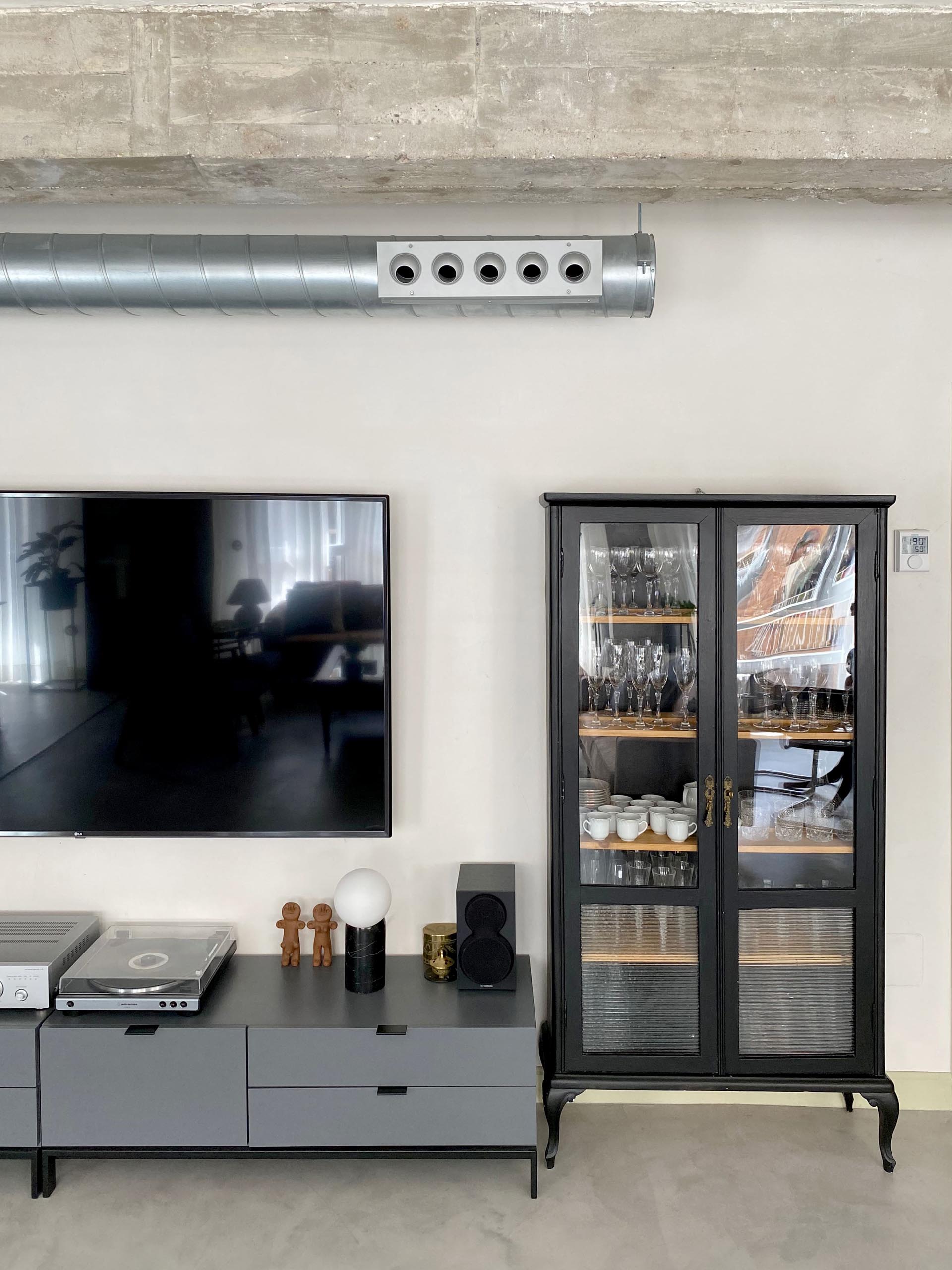 This modern living room showcases the concrete flooring, and is furnished with leather couches, a pair of armchairs, and a wood coffee table. On the living room wall, there's a low console and glass front cabinet that complements the black framed doors.