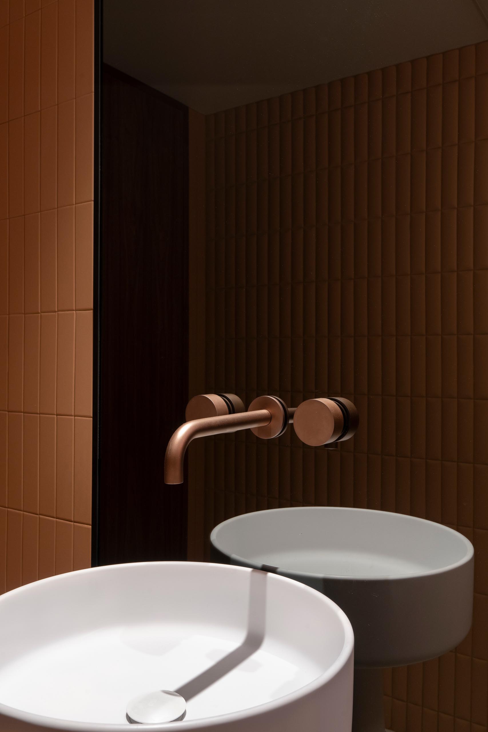 This modern powder room features smoked glass, copper faucets, Italian pedestal washbasin, and terracotta ceramics reminiscent of upholstered leather create a chic appearance.