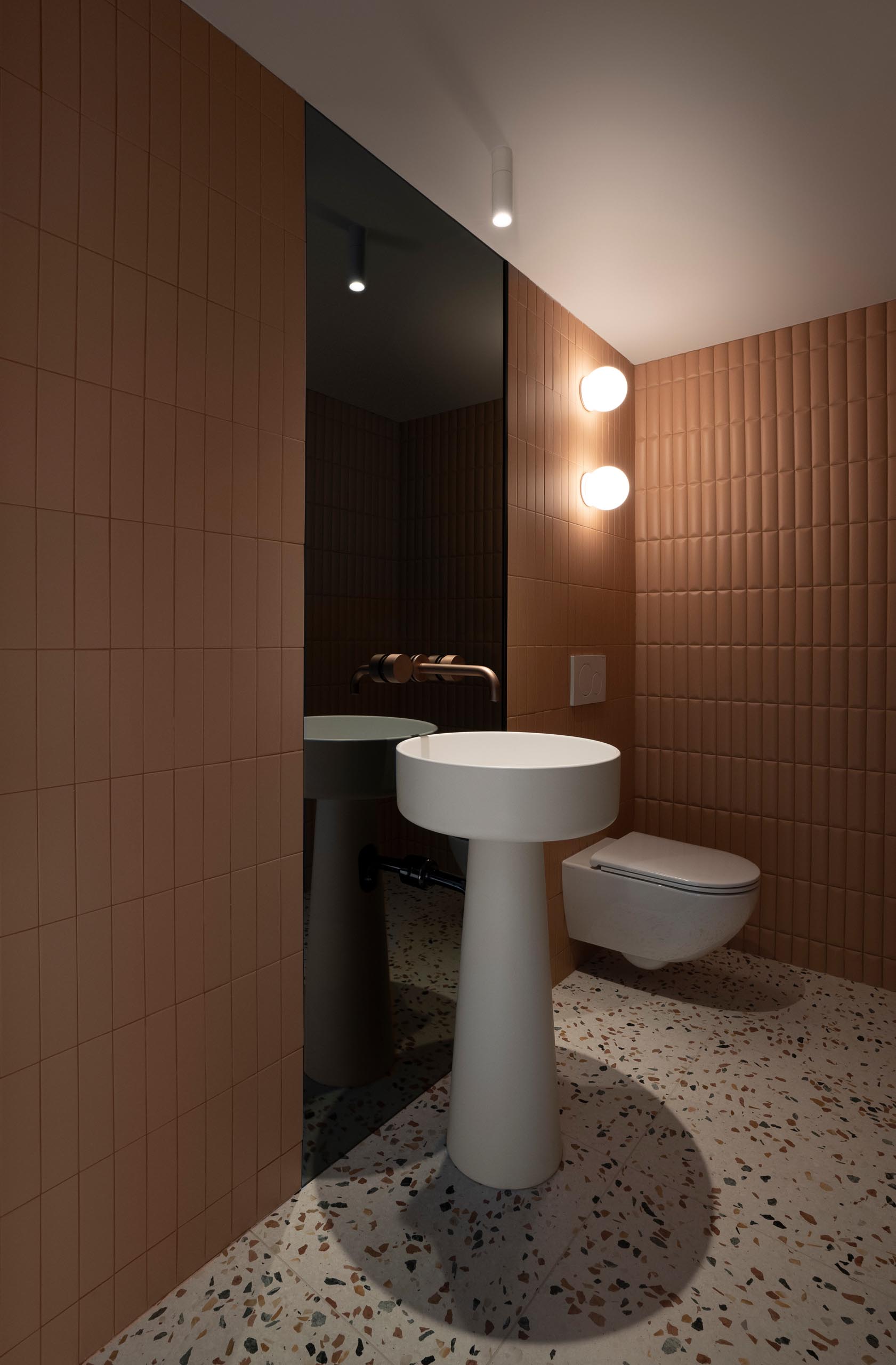 This modern powder room features smoked glass, copper faucets, Italian pedestal washbasin, and terracotta ceramics reminiscent of upholstered leather create a chic appearance.