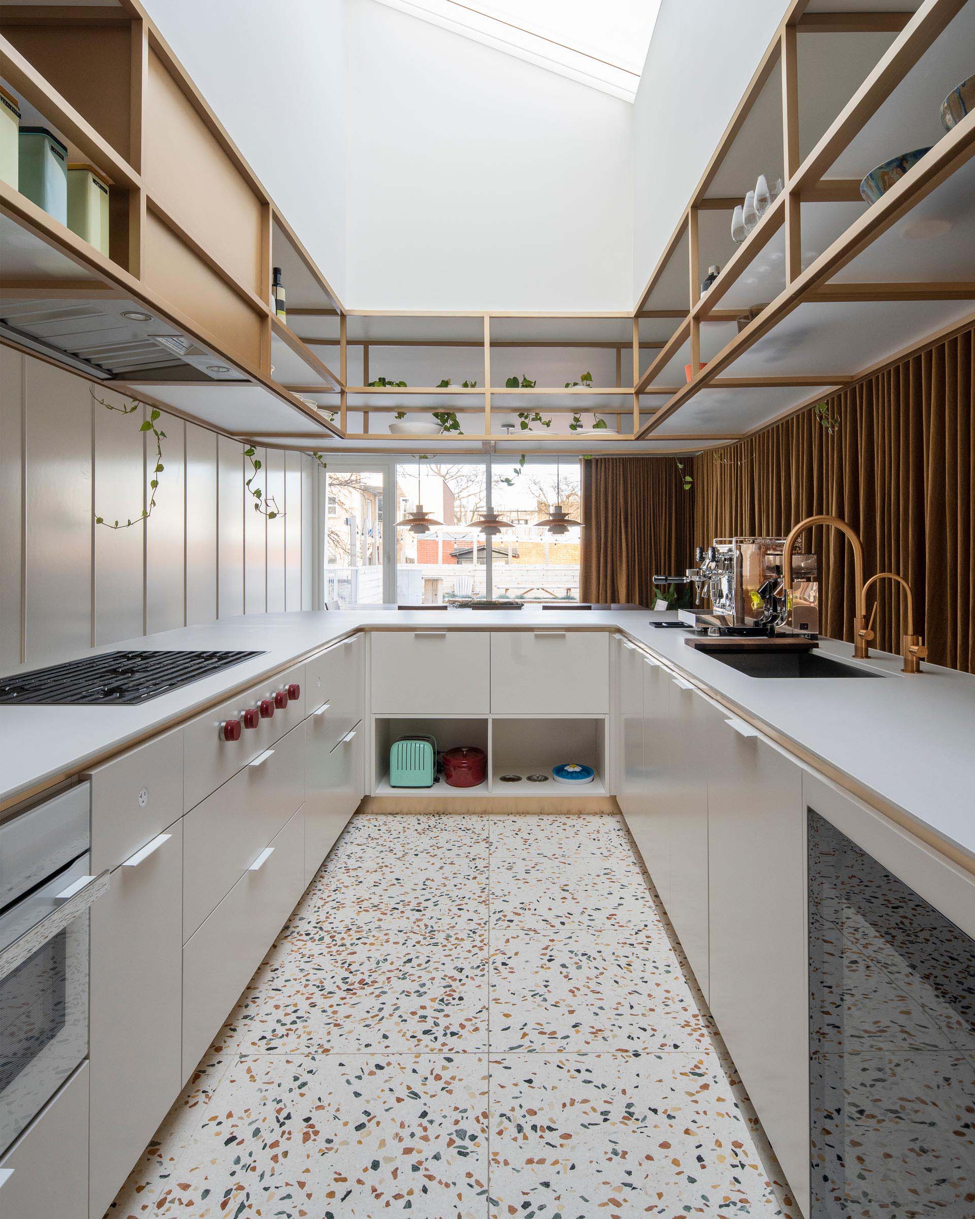 This modern U-shaped kitchen has a terrazzo tile floor, and an elegantly curved countertop with matching upper shelves that are open for easy access.