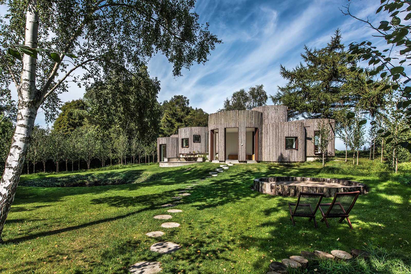 A modern house with a curved cylindrical design, and a wood exterior made from narrow spruce branches.