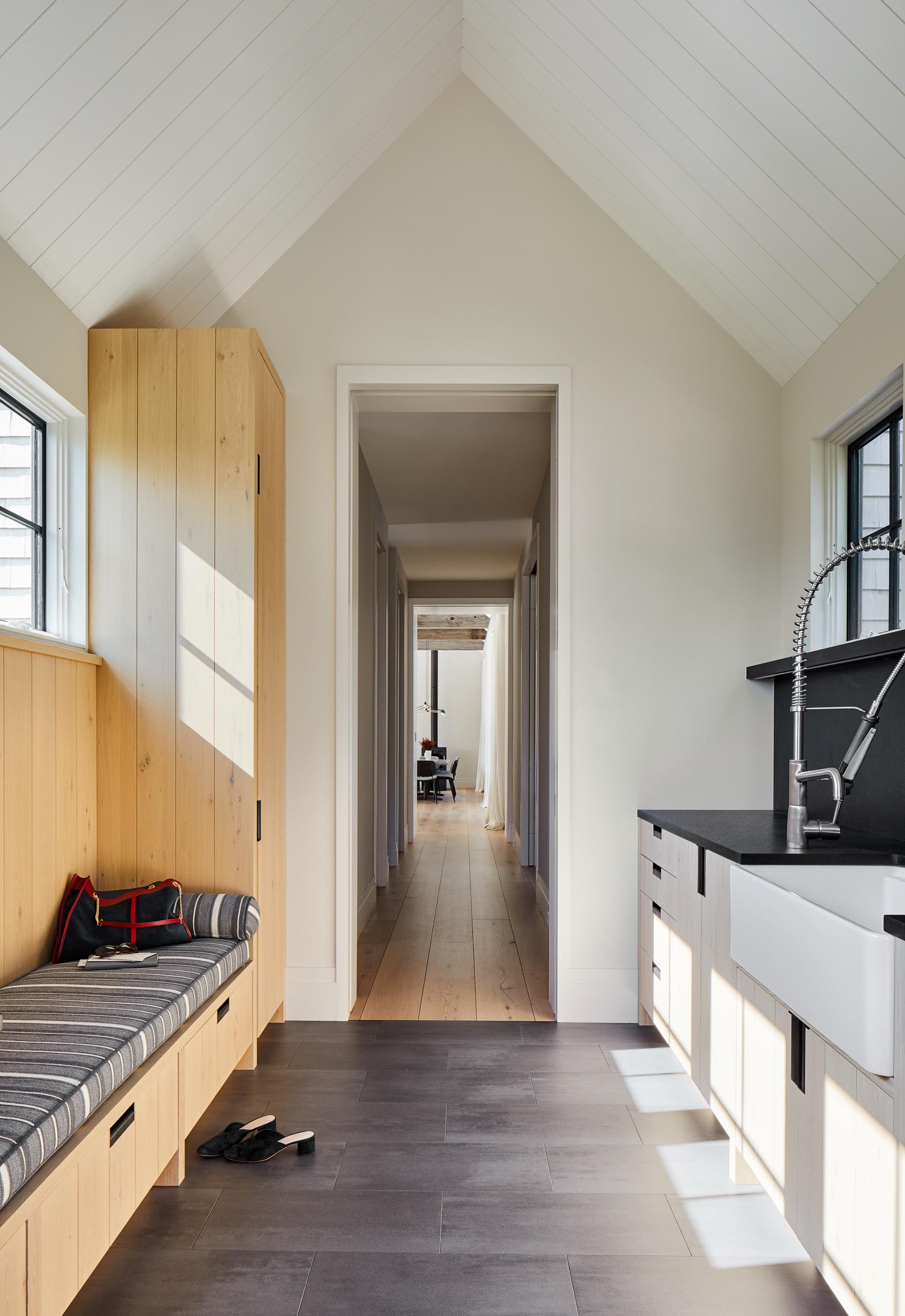 A mud room with a pitched ceiling, a wood bench and cabinet, and a farmhouse sink.