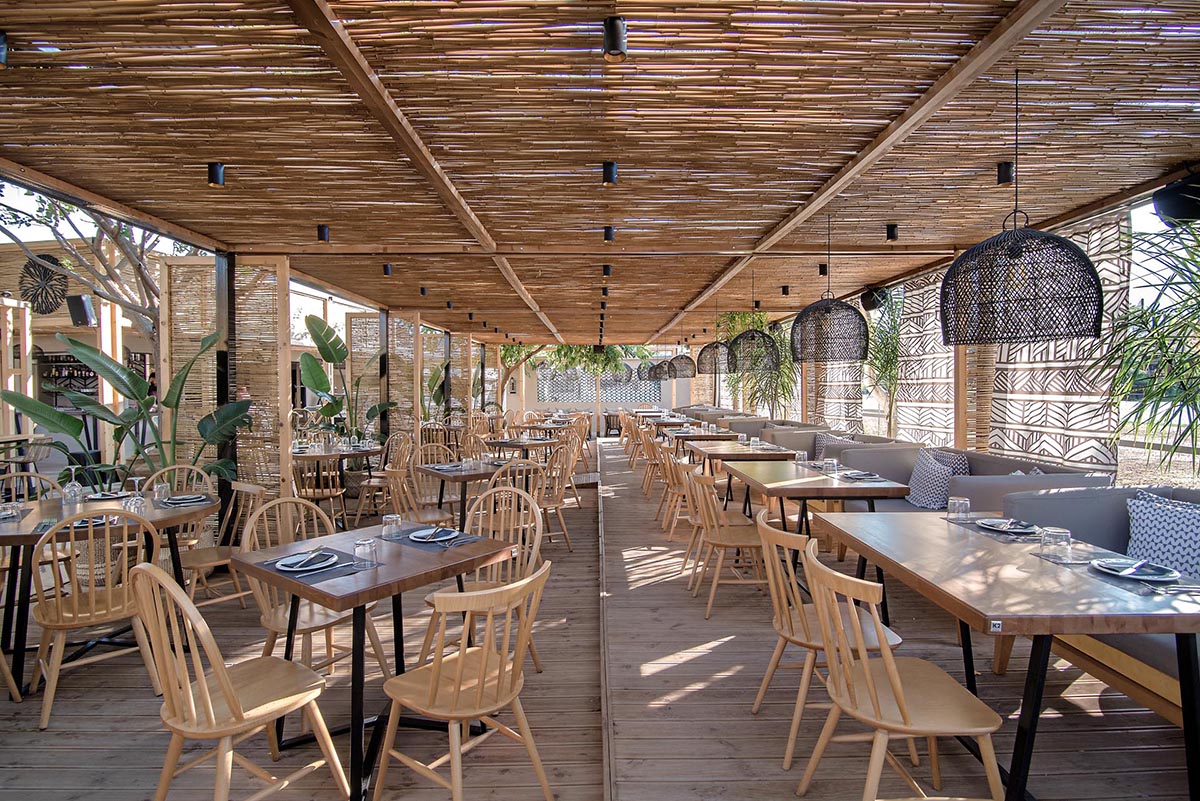 A modern outdoor restaurant with reed screens that provide shade and create a beach aesthetic.