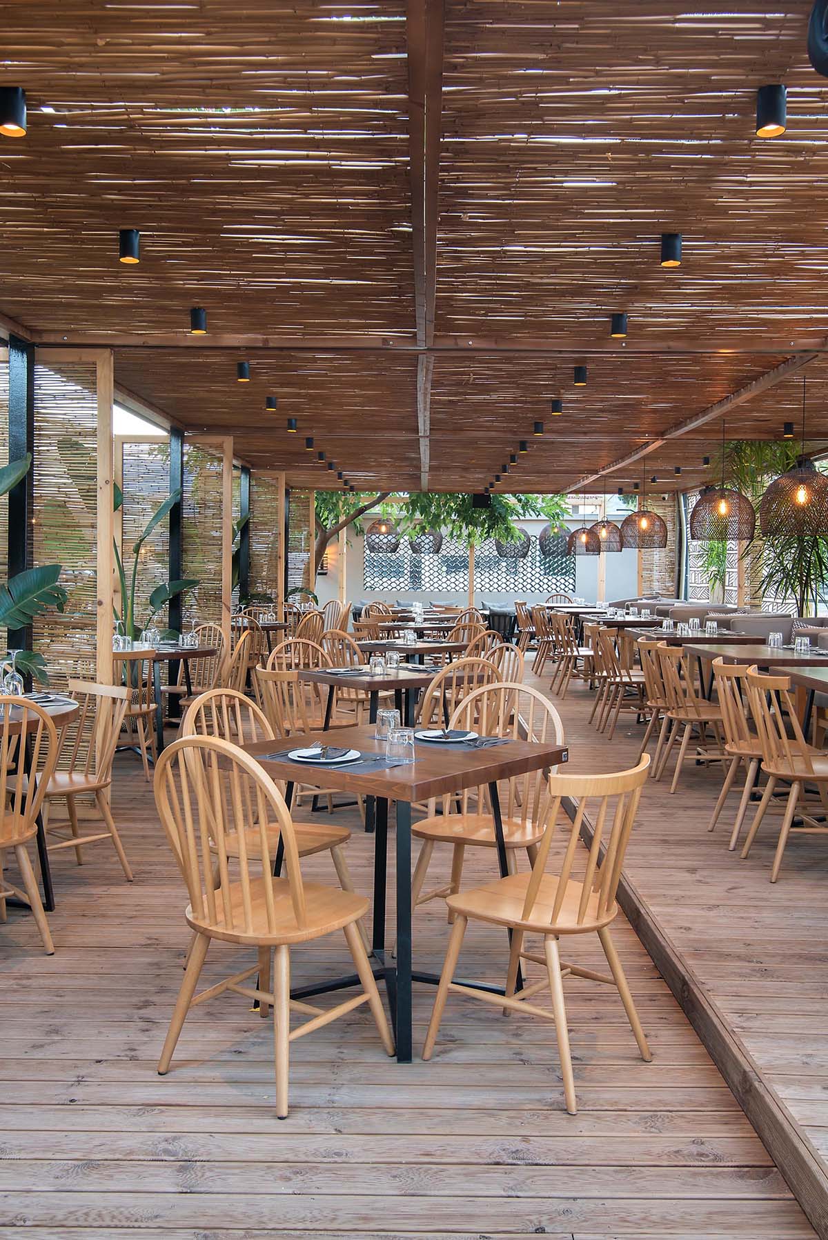 A modern outdoor restaurant with reed screens that provide shade and create a beach aesthetic.