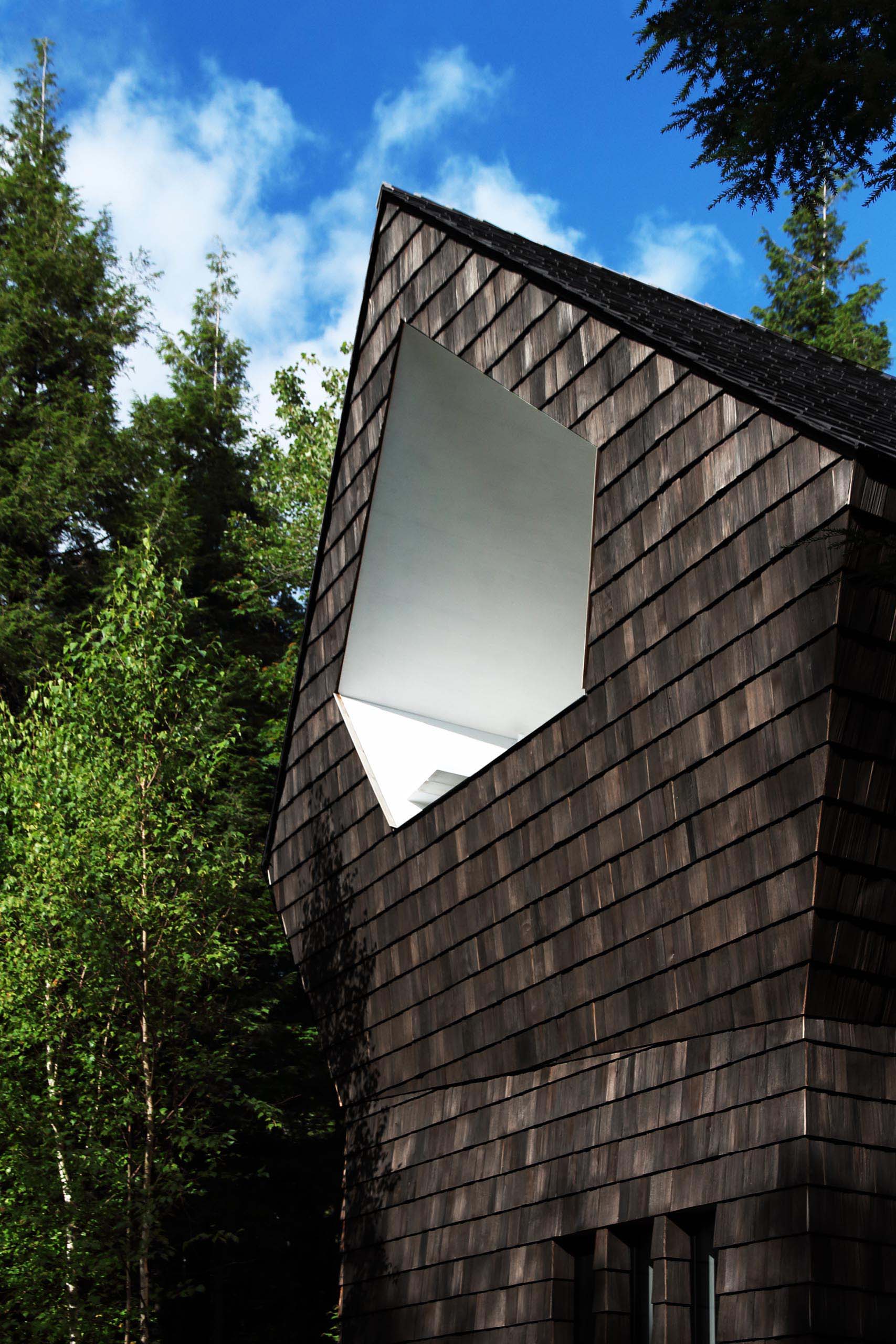 A small wood shingle cottage with a pentagonal shaped terrace that's recessed into the wood shingle clad building.
