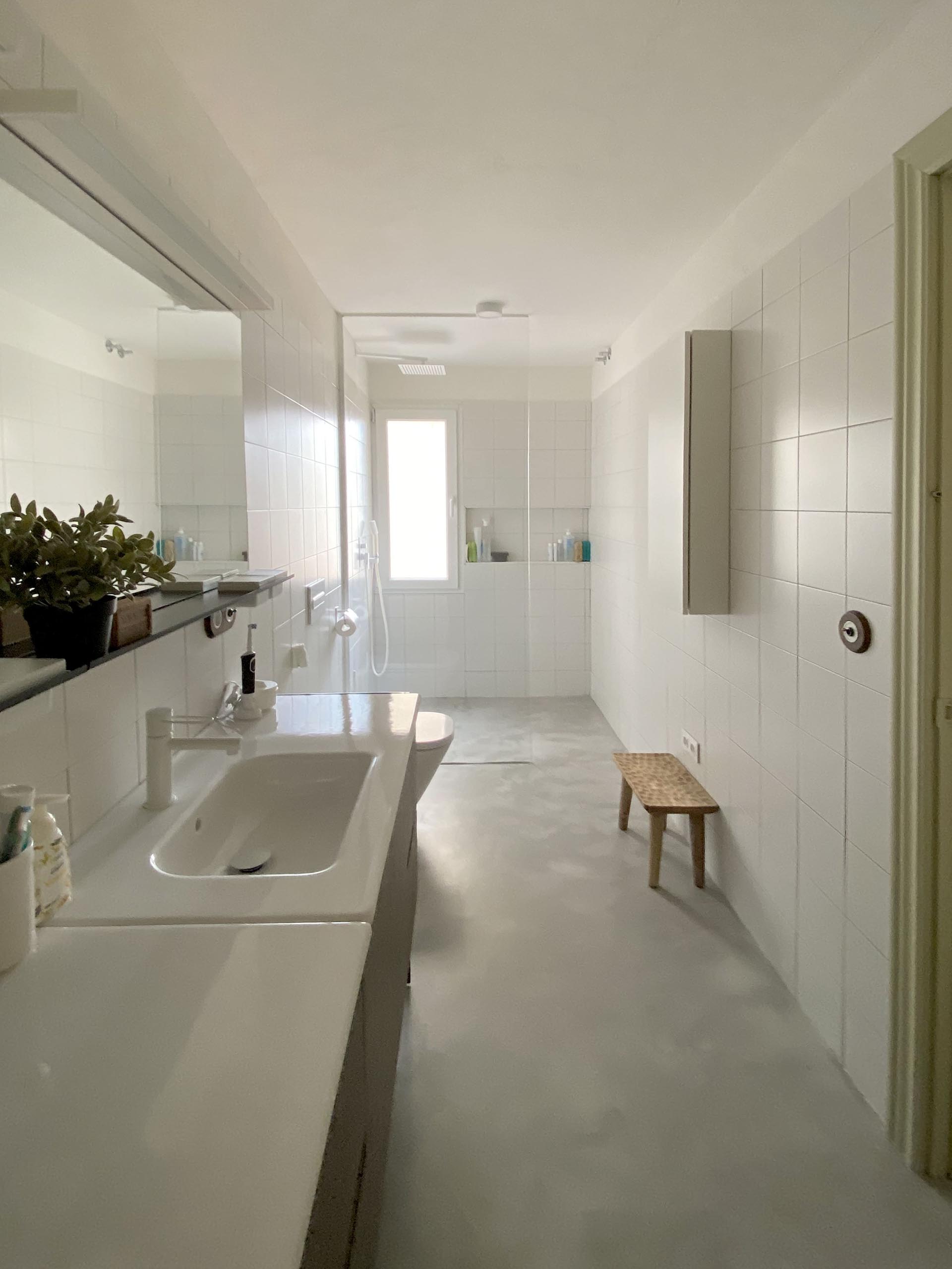 In the bathroom, a dark wood vanity is topped with dual sinks, while square white tiles cover the walls and shower.