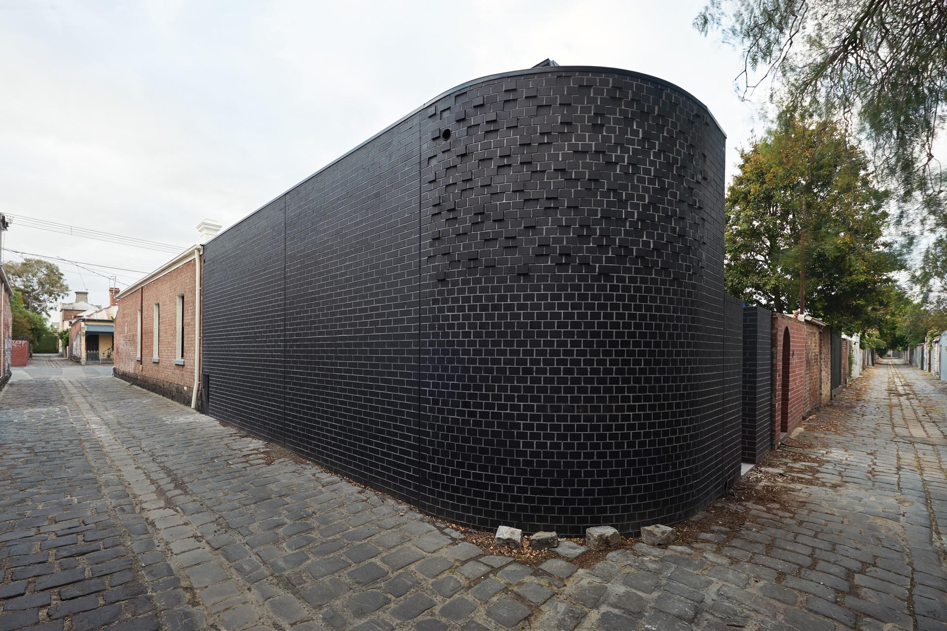 The newly built rear of this traditional Australian home can be seen down the lane at the side of the home and features a black brick that curves around the corner.