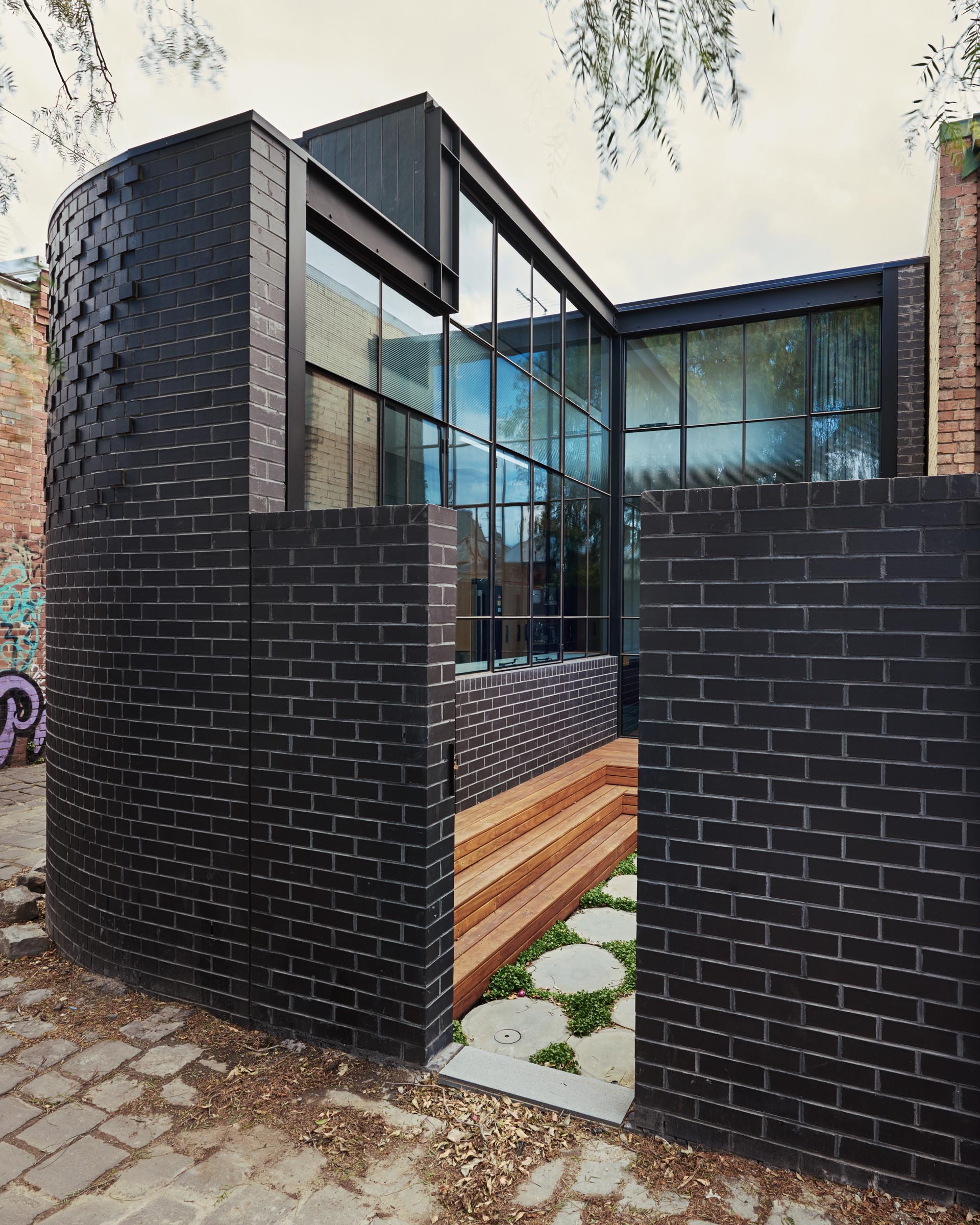 The newly built rear of this traditional Australian home can be seen down the lane at the side of the home and features a black brick that curves around the corner.
