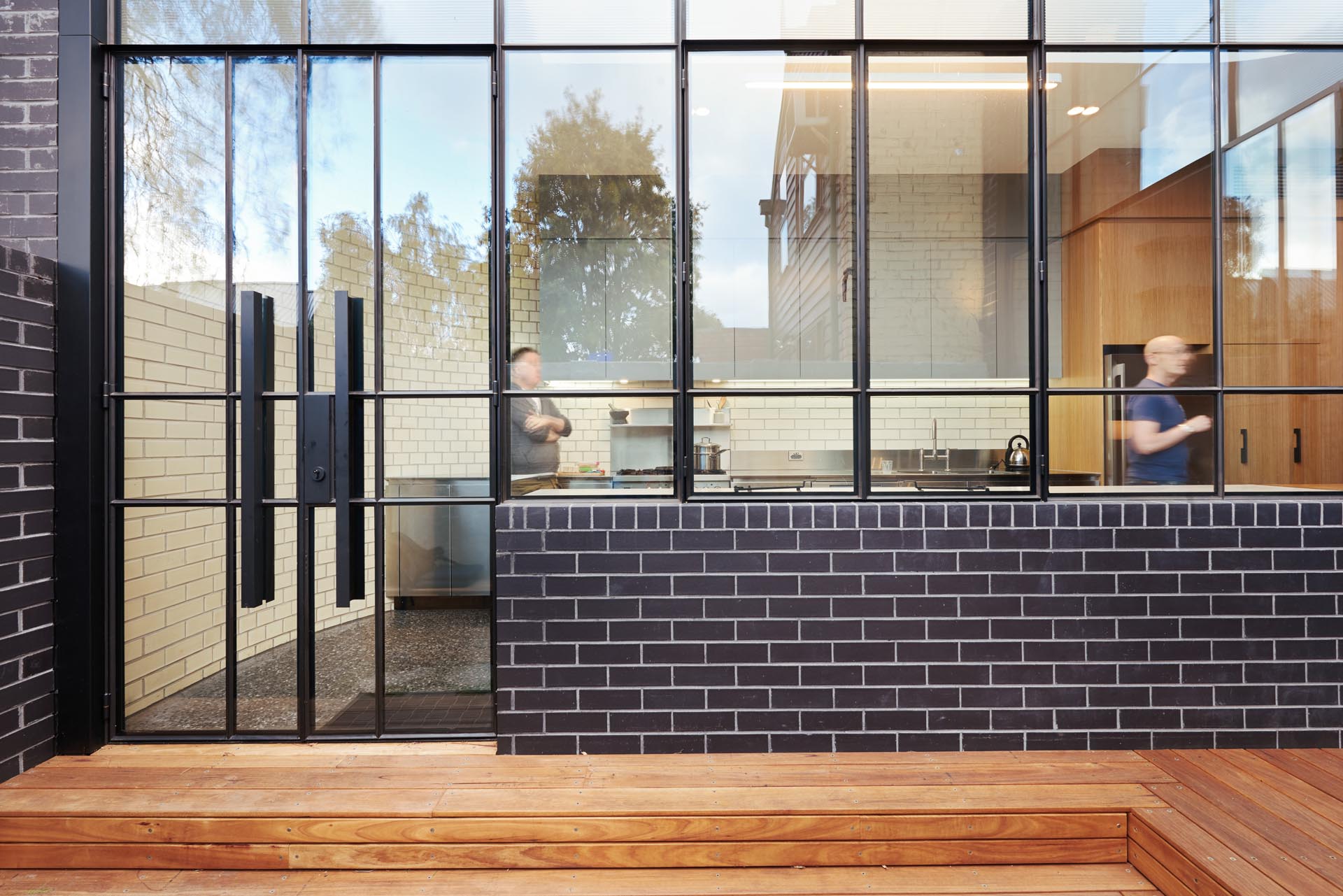 A view of the new kitchen can be seen through a black framed glass wall.