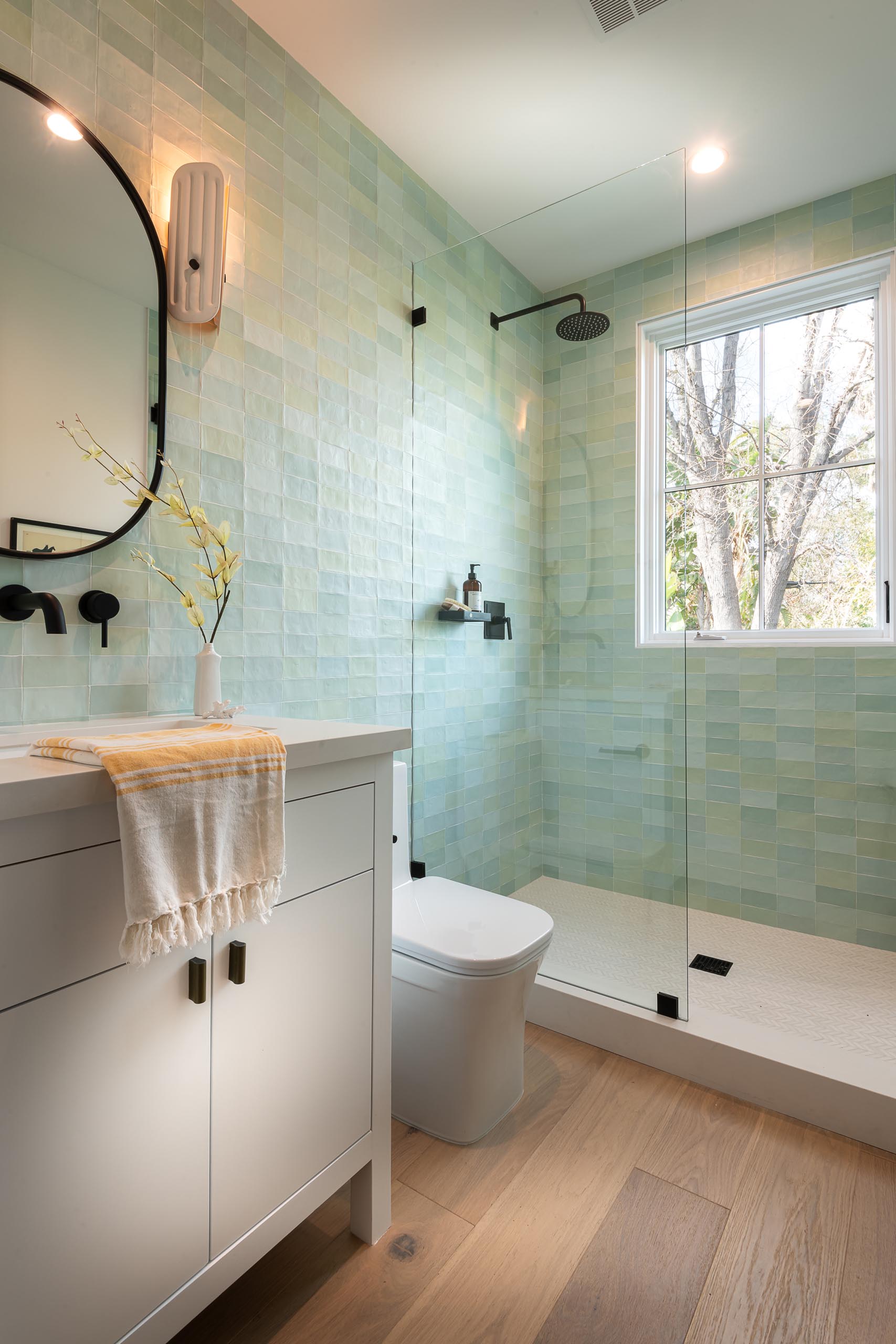 In this bathroom, there's small rectangular tiles in light green and blue tones that cover the walls.