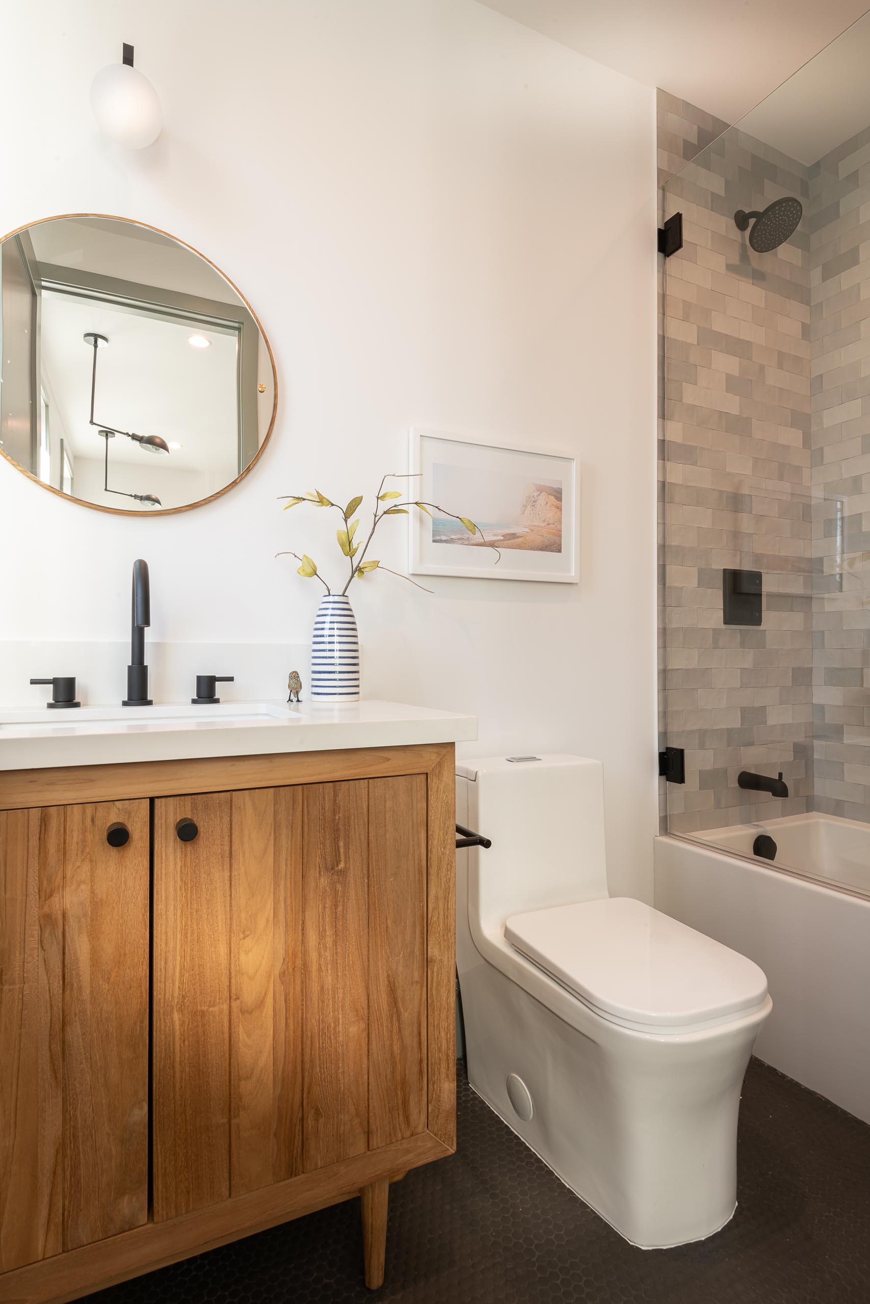 A modern farmhouse bathroom with a rustic wood vanity, round mirror, and black hardware throughout.