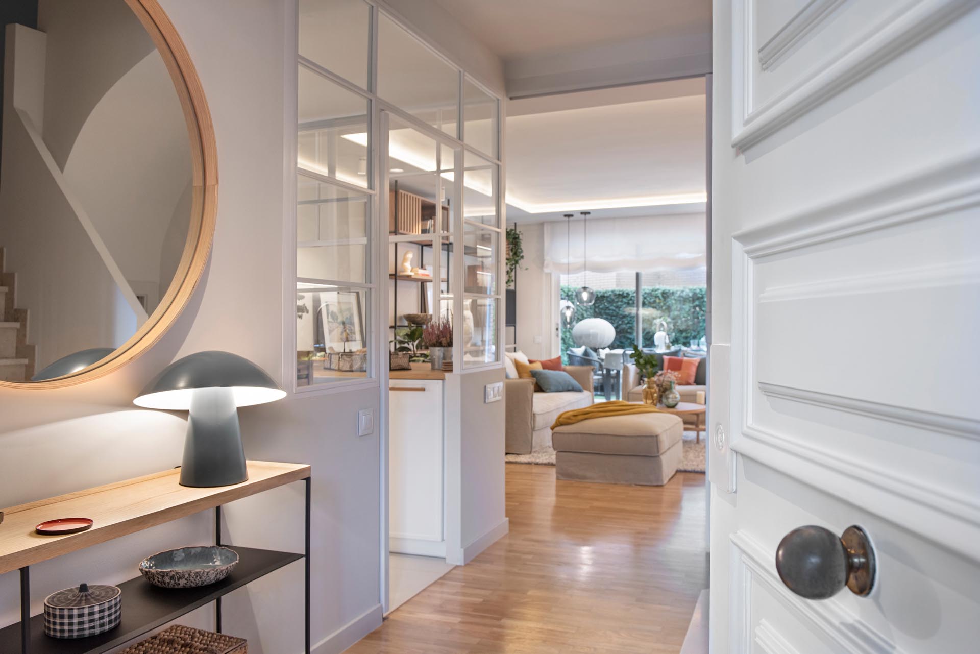 A modern kitchen enclosed within white-framed windows, includes white cabinets that have been paired with a matte green cabinets, while white tiles have been used for the backsplash. An eat-in breakfast nook is tucked into the corner and includes a built-in bench, and a mirrored wall, which makes the space feel larger.