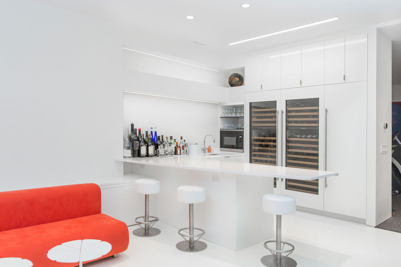 This modern basement bar includes cabinetry has a white lacquer finish, while the white Caesarstone countertop complements the white resin floors.