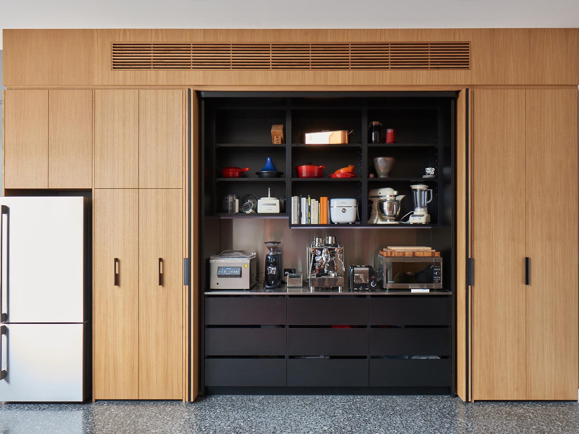 A coffee station is hidden within this modern wood cabinetry, that also includes built-in black shelving and drawers.