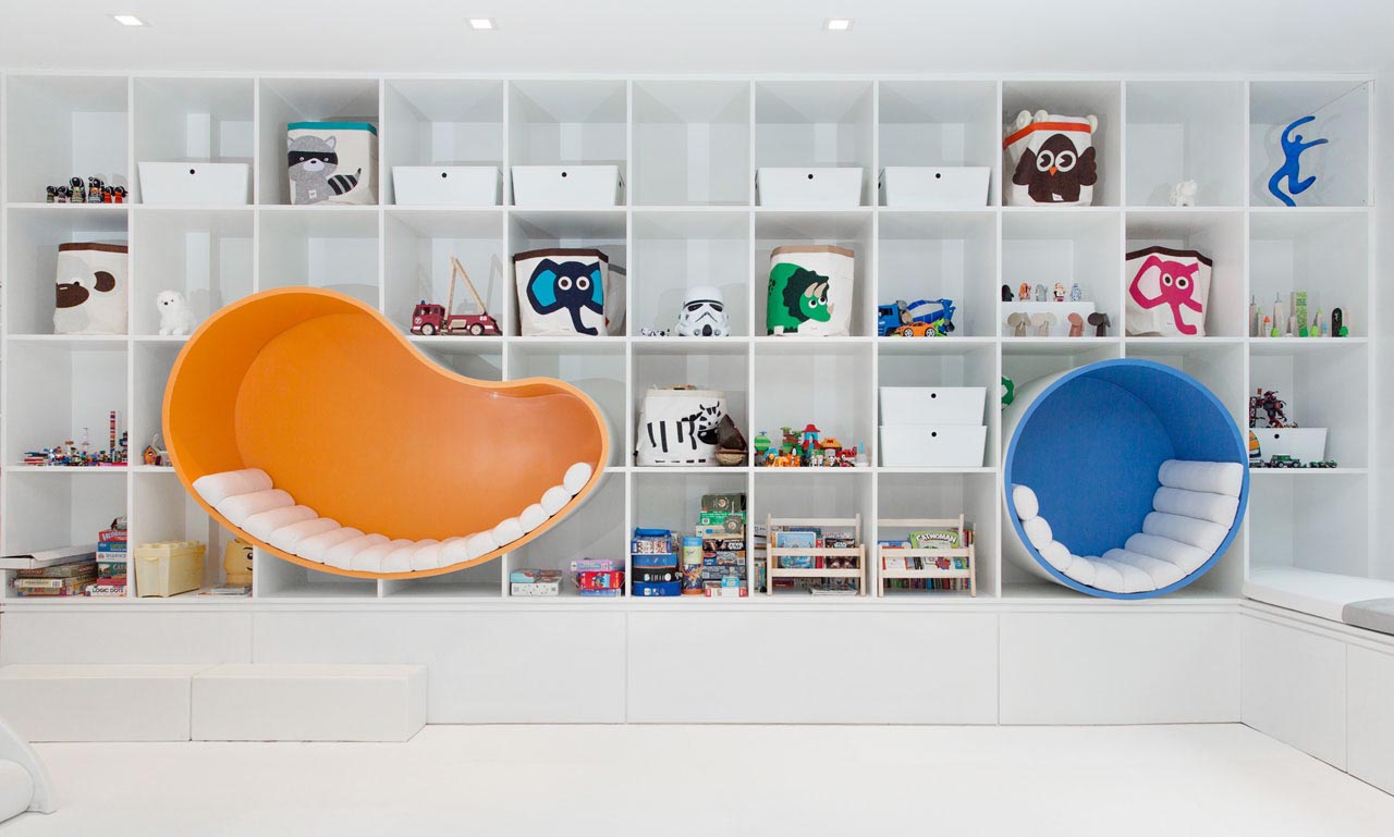 A wall of storage with square shelves provides plenty of storage for the space, while bright and colorful seating nooks are lined with padded cushions.