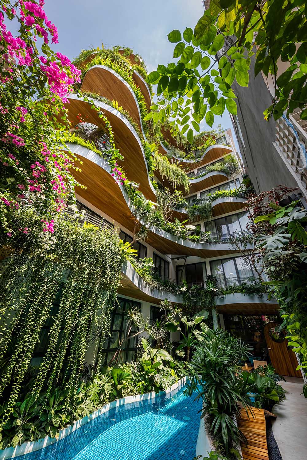 A modern building with curved balconies and overhanging plants.