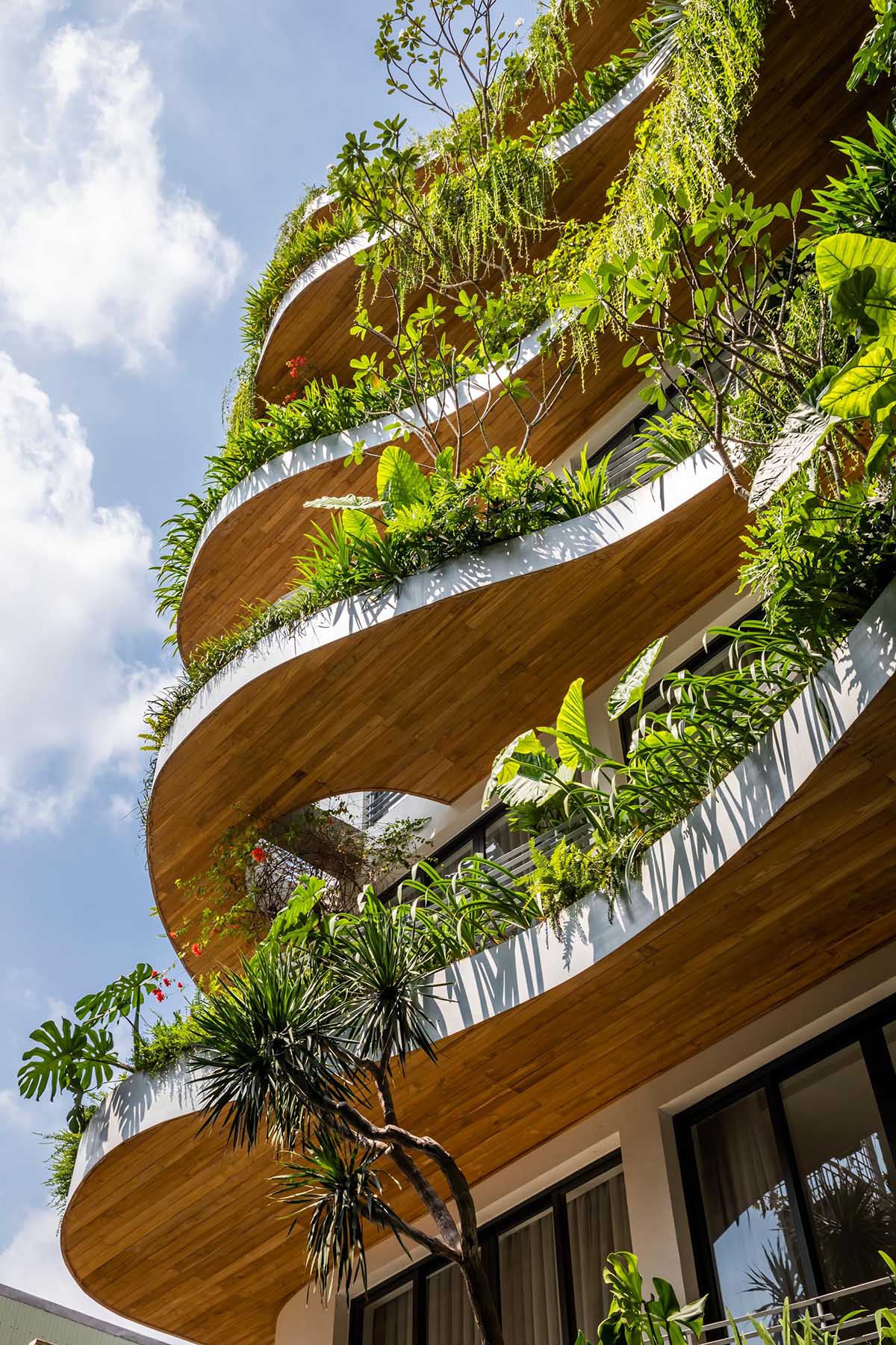 A modern building with curved balconies and overhanging plants.