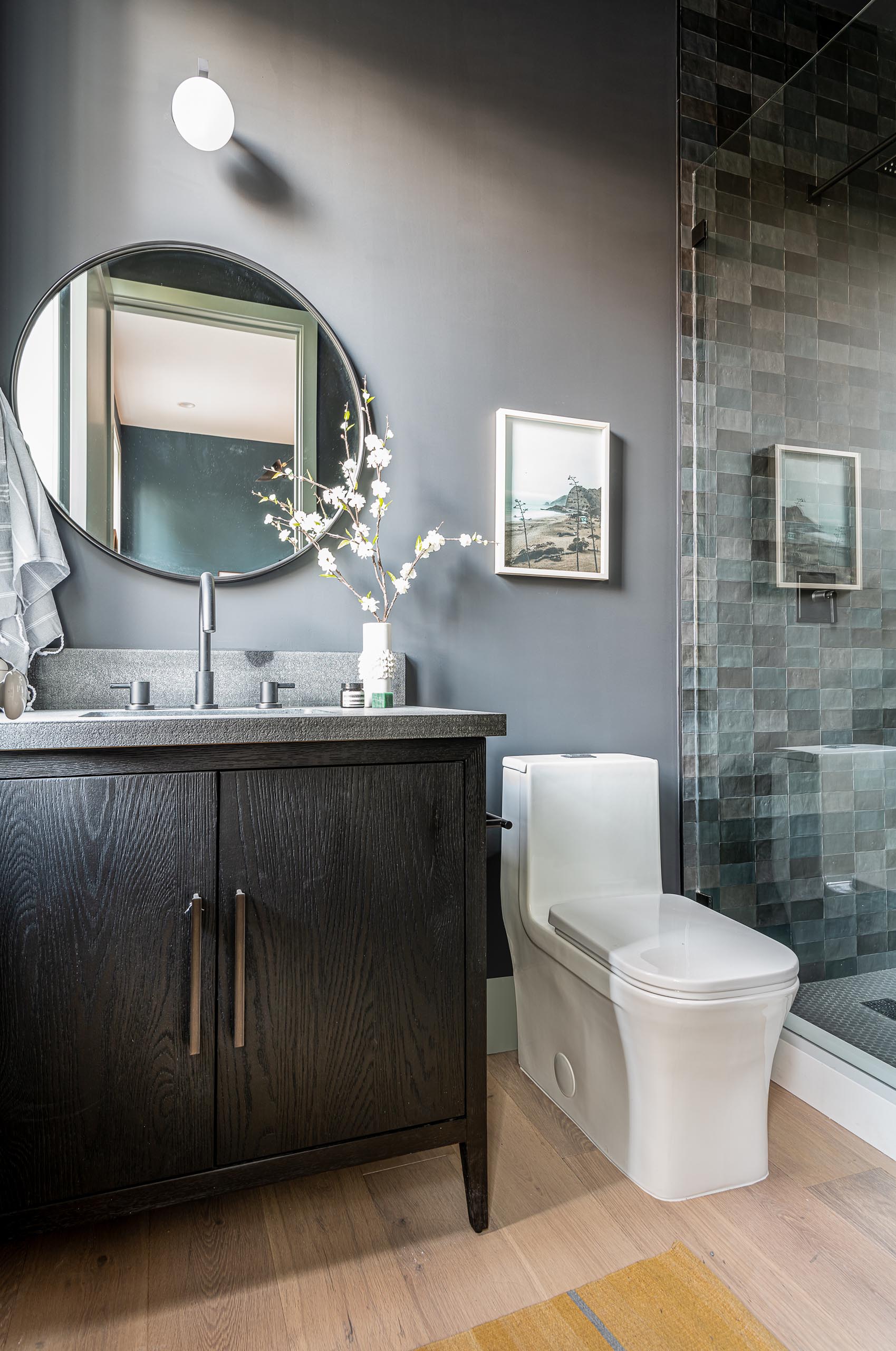 A modern bathroom with light gray walls, a round mirror, and a dark wood vanity.