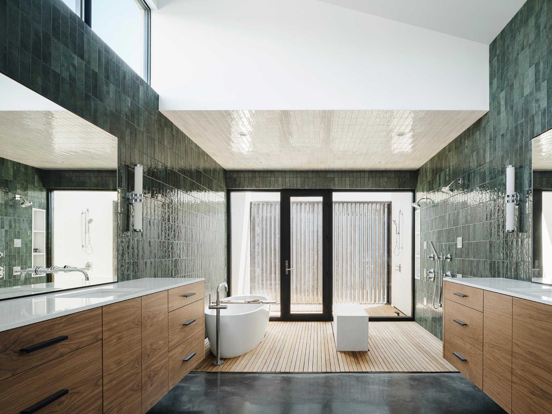 A modern bathroom with a naturally lit shower and bathing area that opens out to an outdoor shower, screened from the nearby neighbor with a custom steel slatted wall. Glazed green wall tiles have been used to create a unique look for the bathroom.