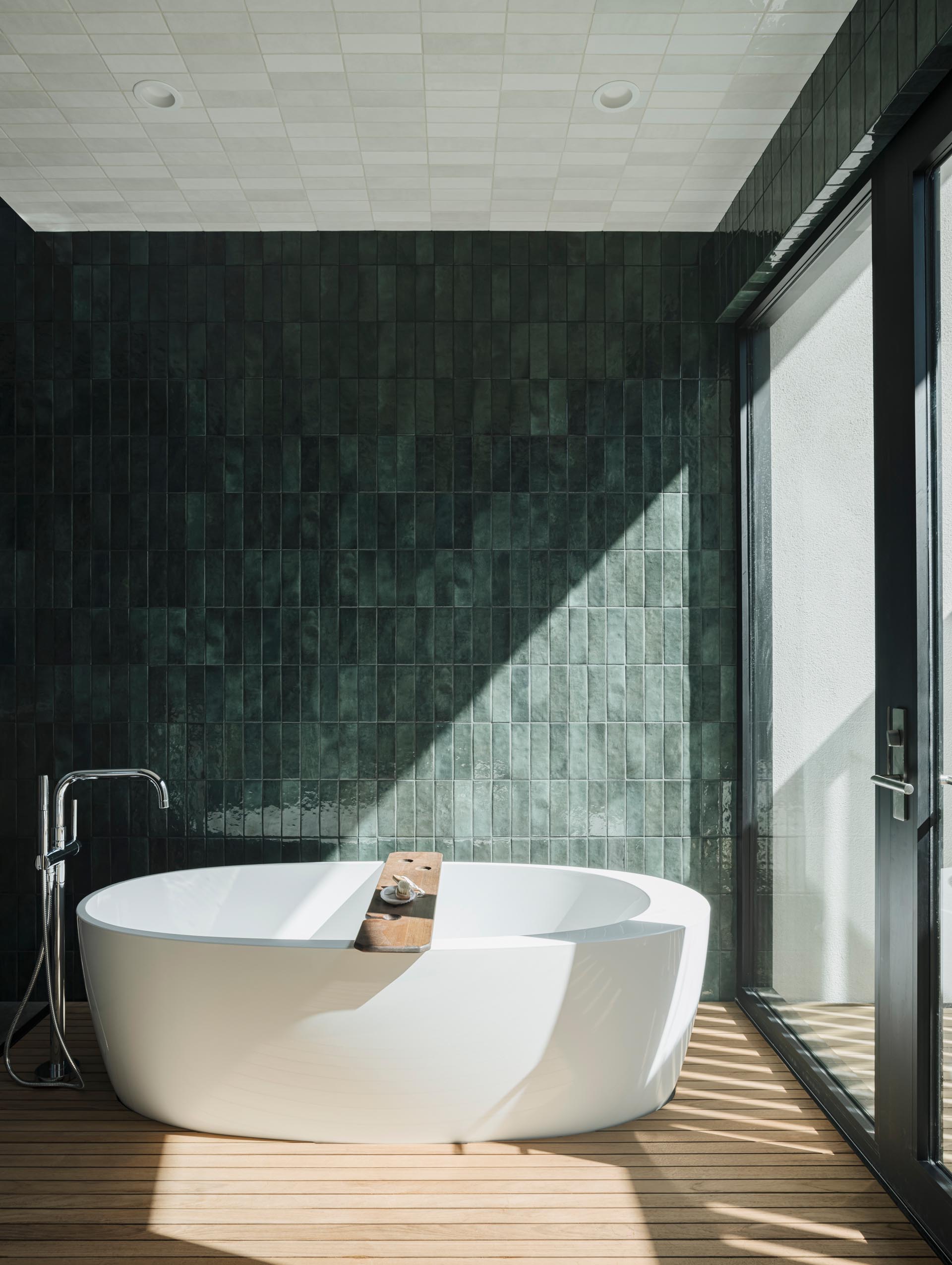 A modern bathroom with a naturally lit shower and bathing area that opens out to an outdoor shower, screened from the nearby neighbor with a custom steel slatted wall. Glazed green wall tiles have been used to create a unique look for the bathroom.