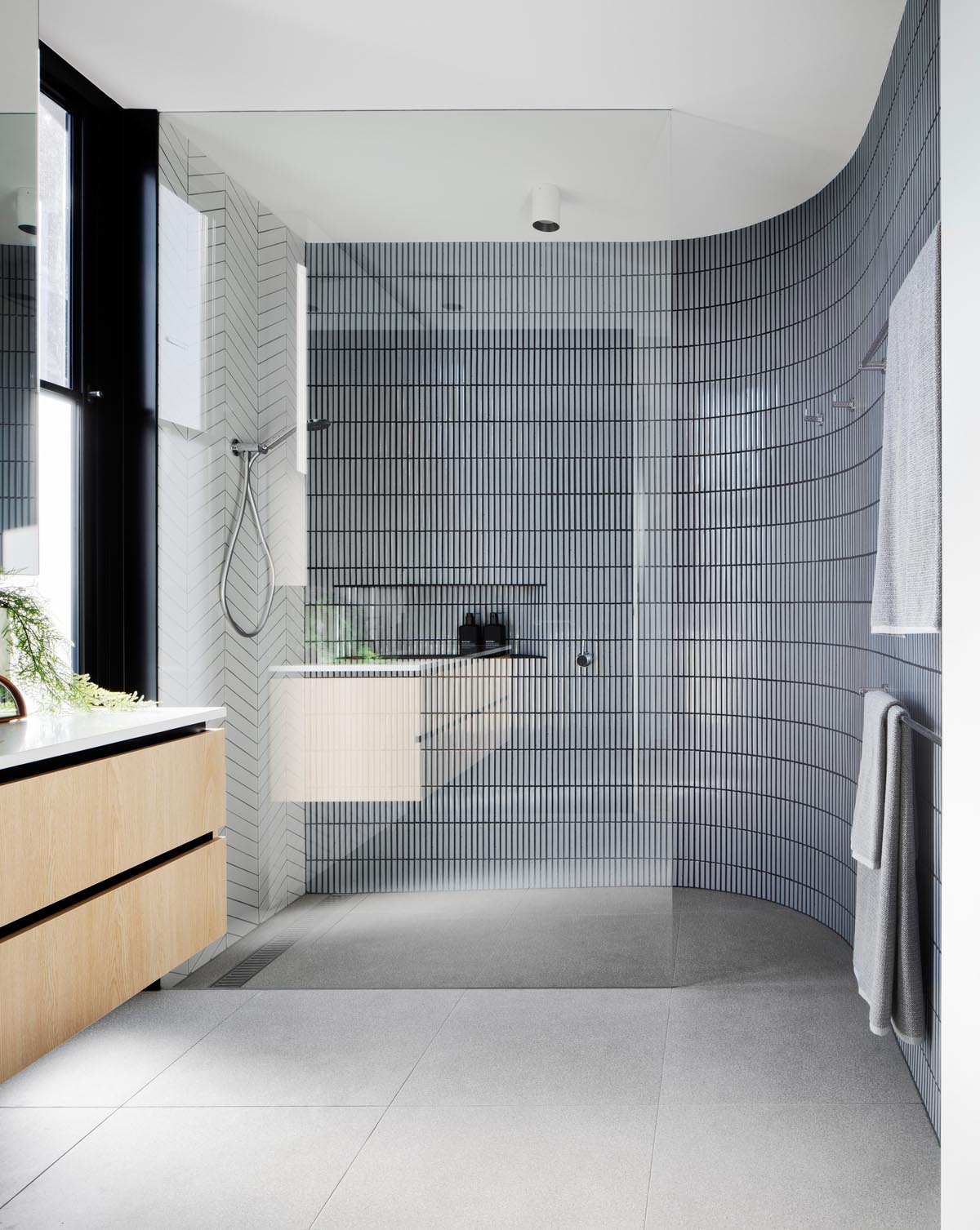 In this modern bathroom, there's two types of tiles that cover the walls in the shower, with a white tile in a chevron pattern, and a small gray tile laid in a vertical pattern.