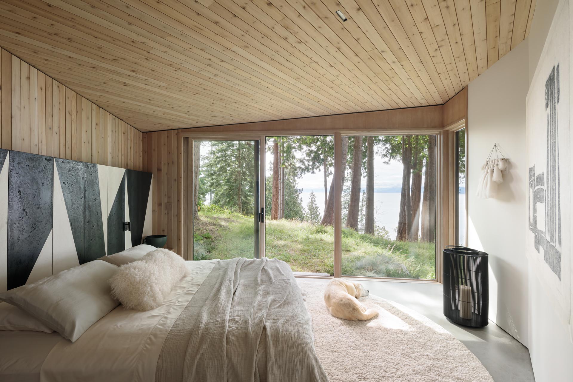 This modern bedroom makes the most of the view by having a wall of windows, while a black and white partial accent wall wraps around the room, and adds an artistic element to the space.