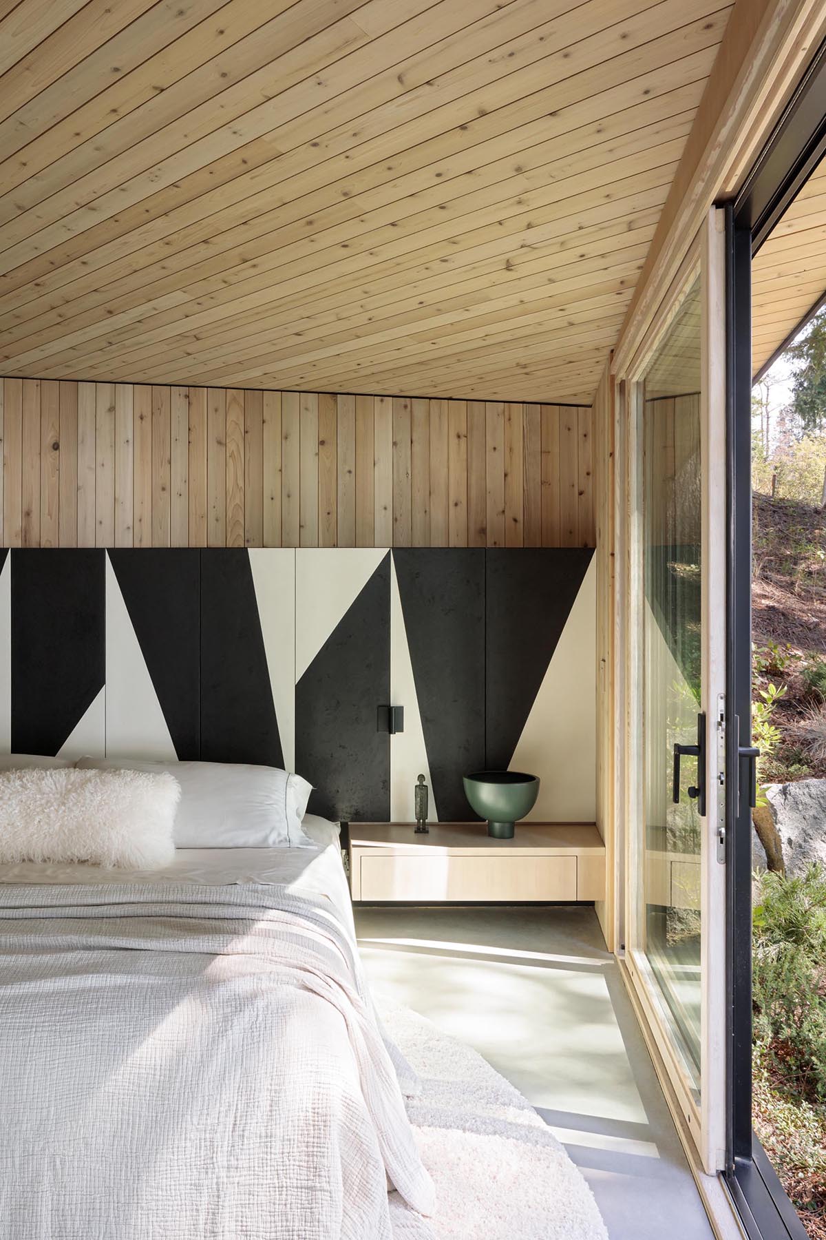 This modern bedroom makes the most of the view by having a wall of windows, while a black and white partial accent wall wraps around the room, and adds an artistic element to the space.