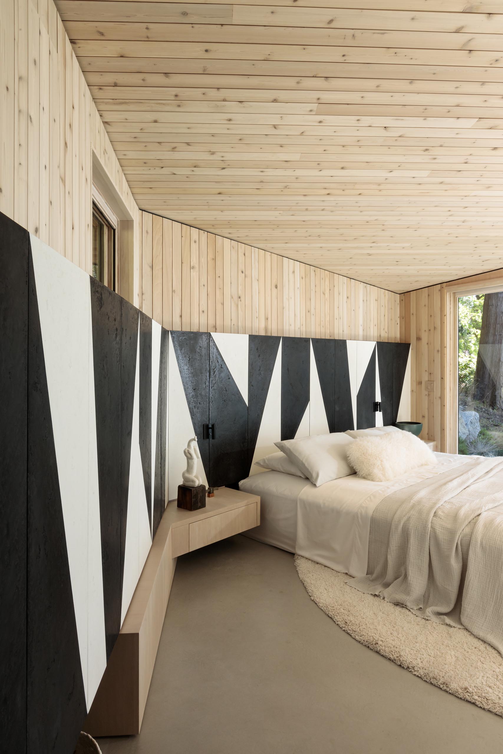 This modern bedroom makes the most of the view by having a wall of windows, while a black and white partial accent wall wraps around the room, and adds an artistic element to the space.