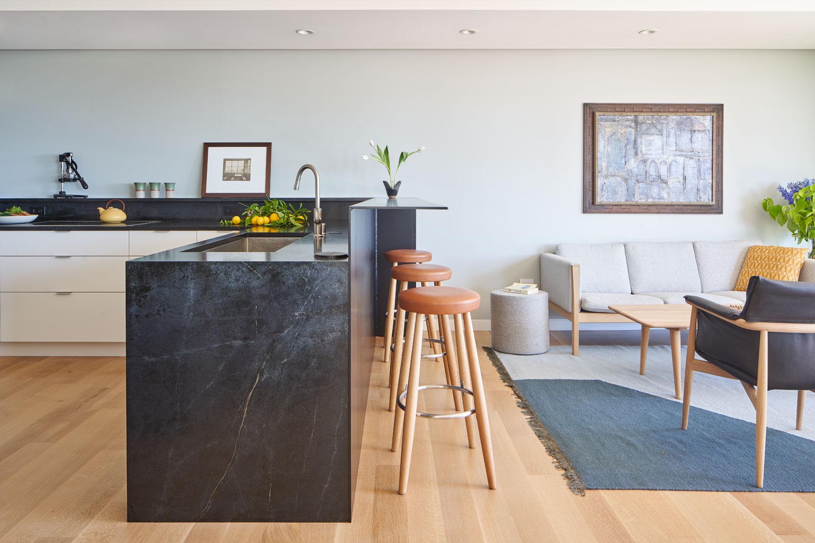 This modern kitchen has been designed with a wall of white cabinetry that wraps around to become lower cabinets, while the dark countertop connects with a raised steel breakfast bar.