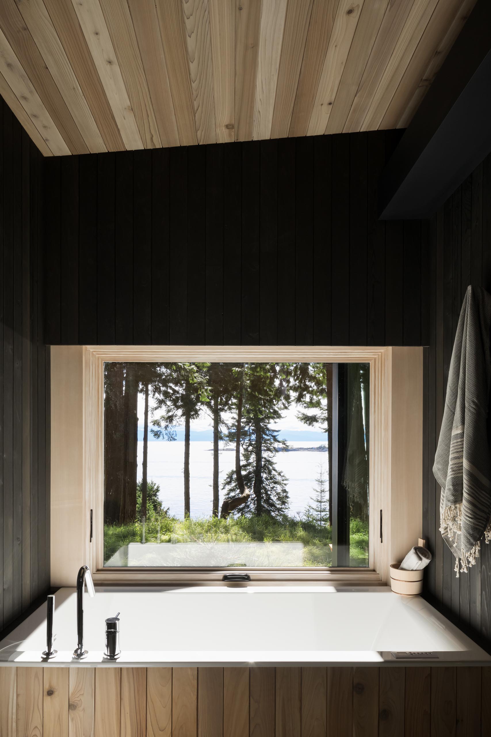 In this modern bathroom, blackened cedar wood walls surround a built-in bathtub.