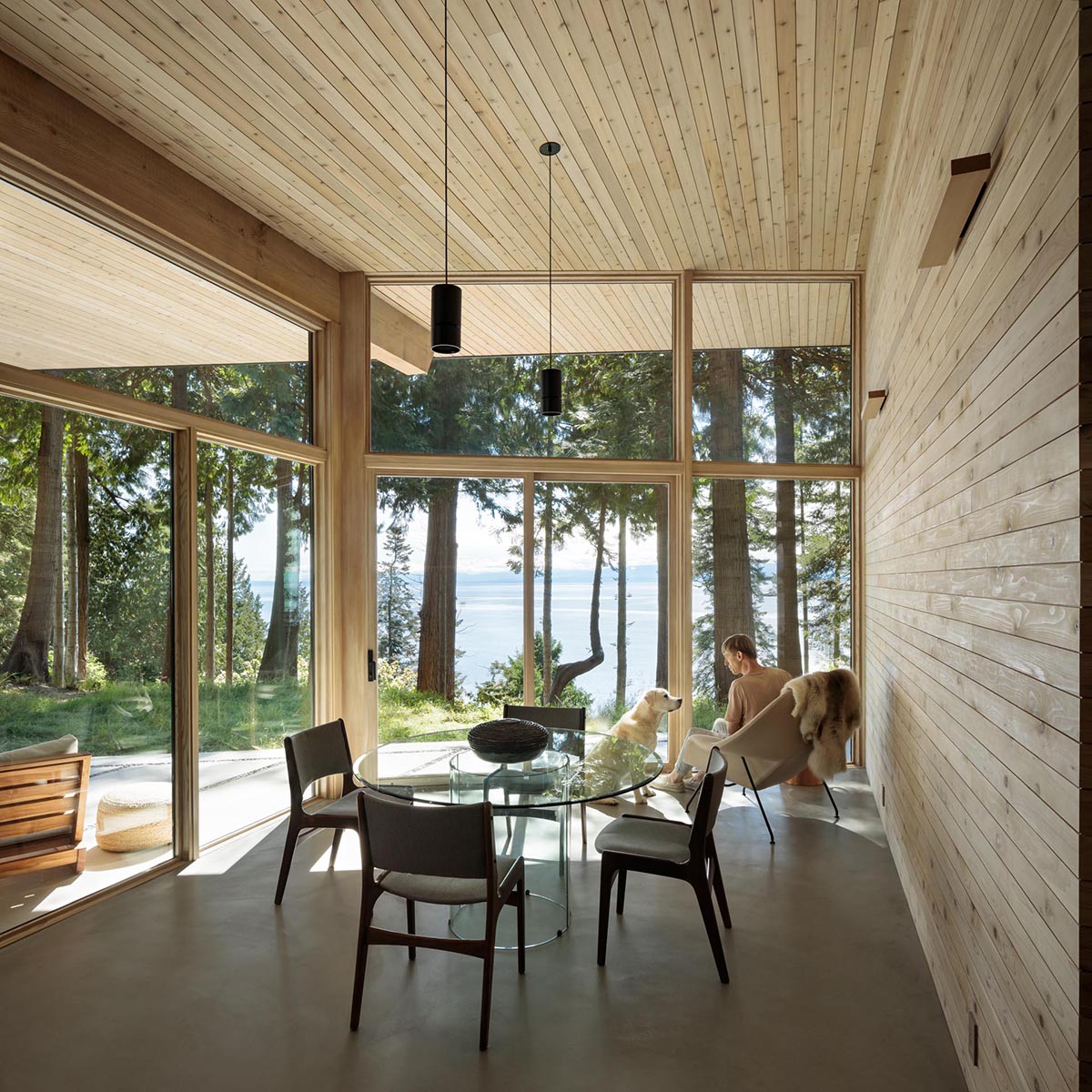 Adjacent to a patio with a fire bowl is the dining room, which has a wood lined wall, and a concrete floor.