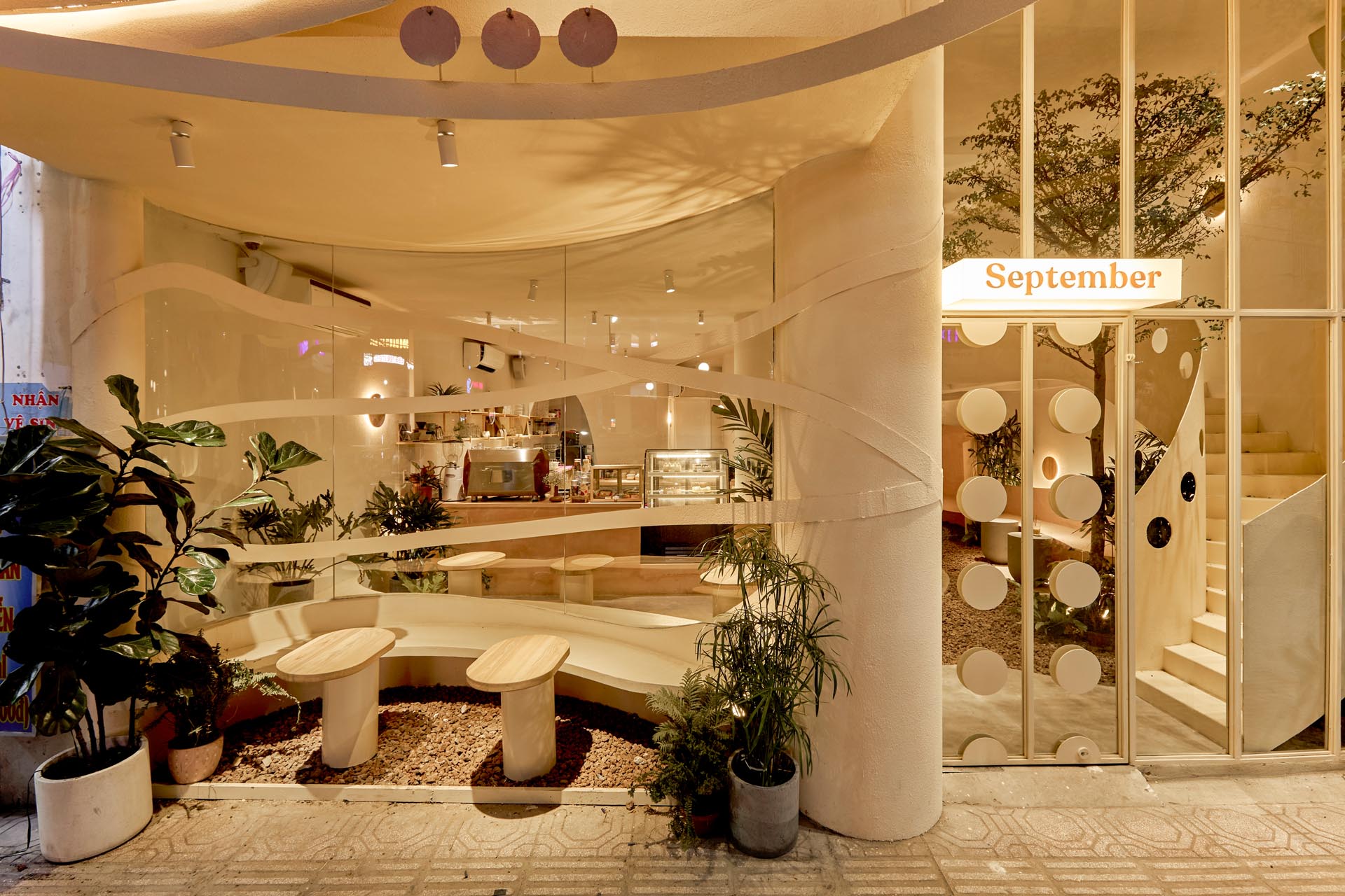 At the front of this modern coffee shop is a curved outdoor seating area that's setback from the sidewalk, while the front door is noticeable due to the circular accents.