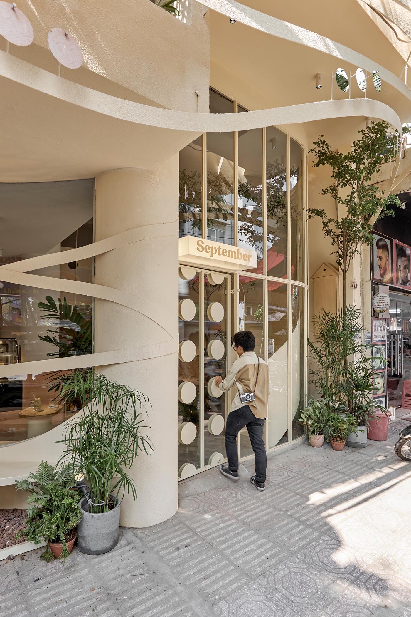 At the front of this modern coffee shop is a curved outdoor seating area that's setback from the sidewalk, while the front door is noticeable due to the circular accents.