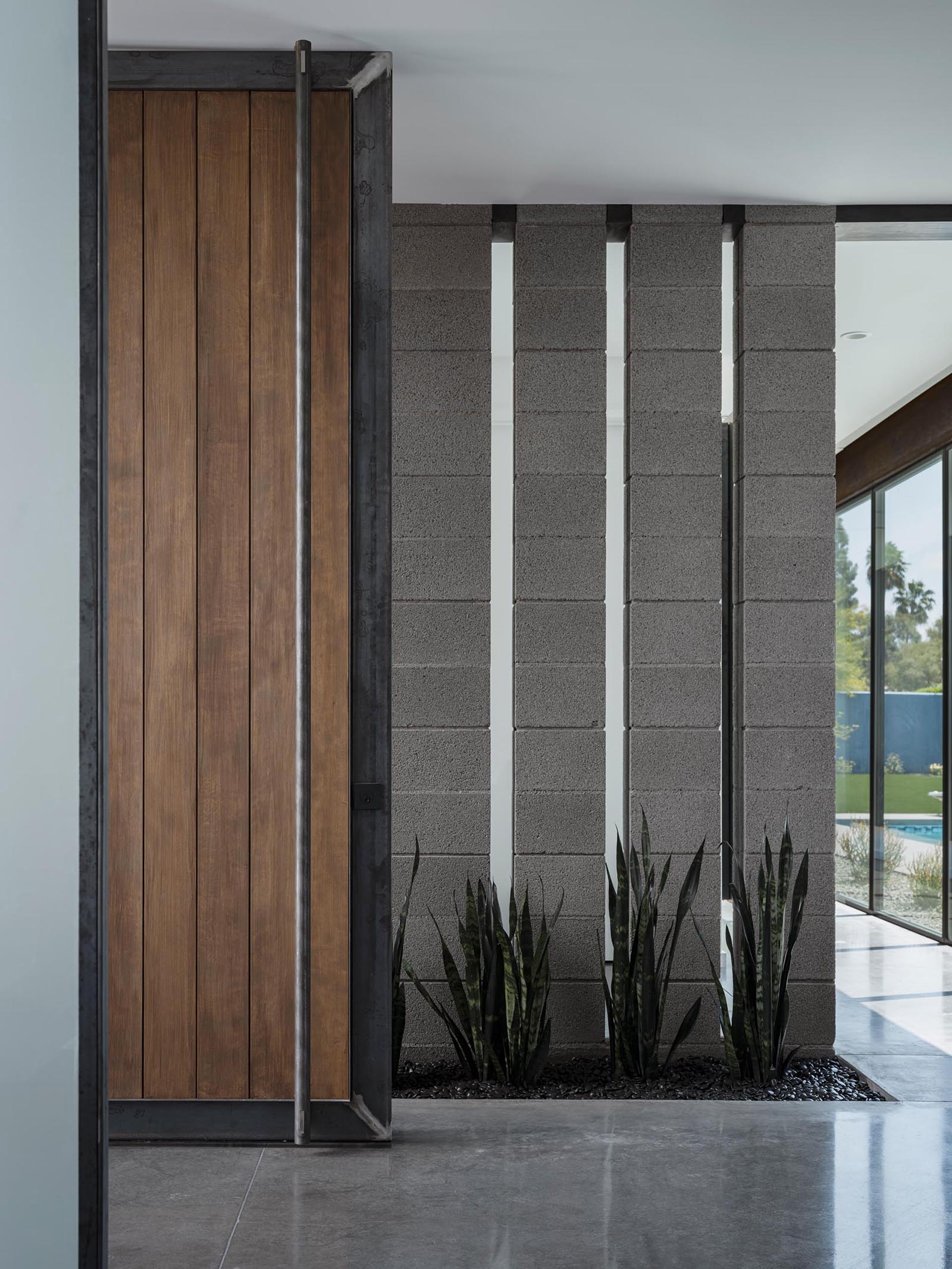 An oversized wood front door with a metal frame pivots to create an eye-catching entryway that opens to a foyer. A small garden is featured on both the exterior and interior of the home.